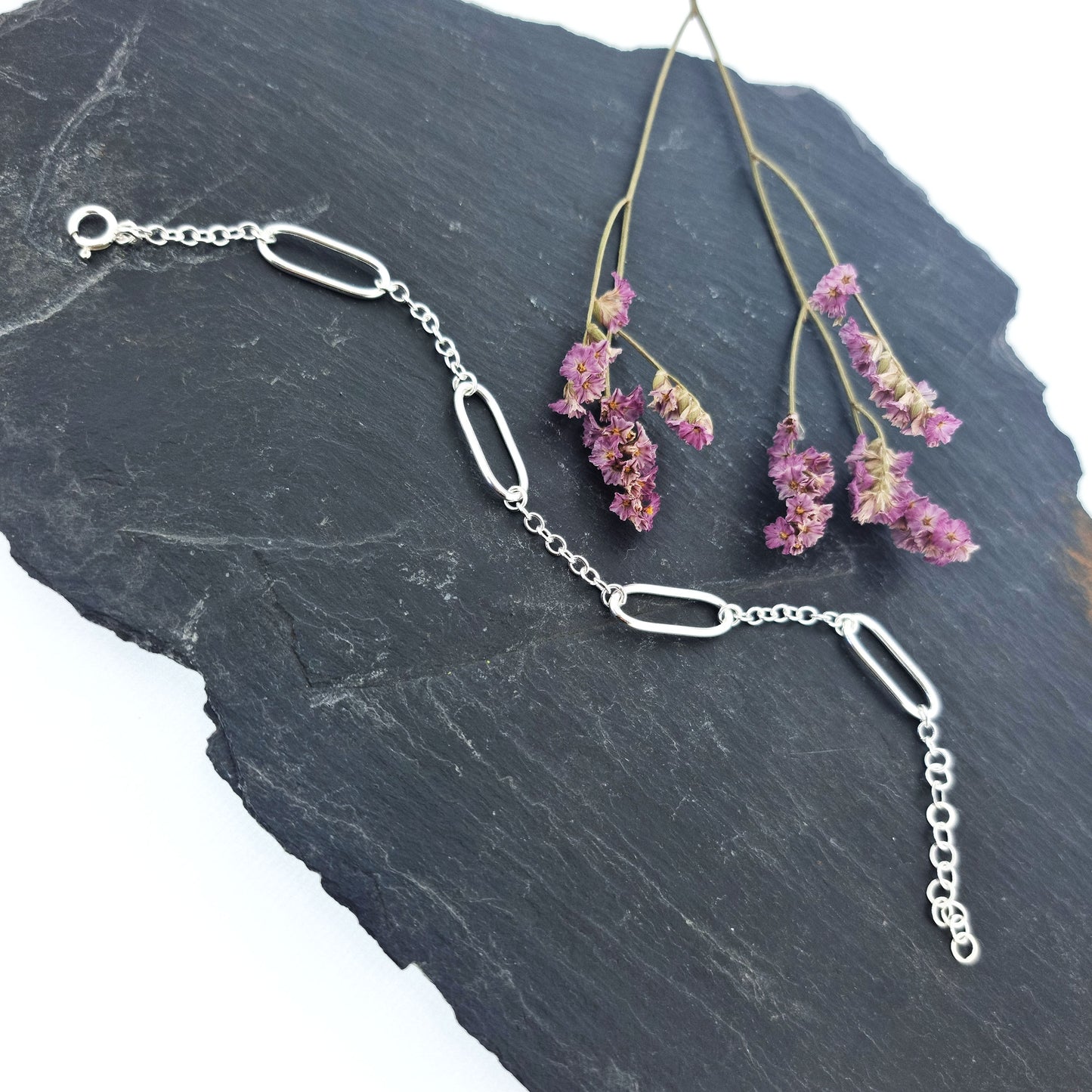 A silver bracelet with 4 oblong oval links set between round linked chain. Pictured on slate with flowers.