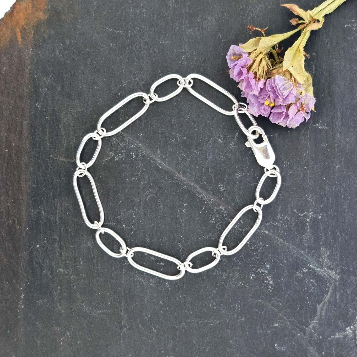 Silver chain bracelet with oblong links of different sizes. Pictured with flowers.