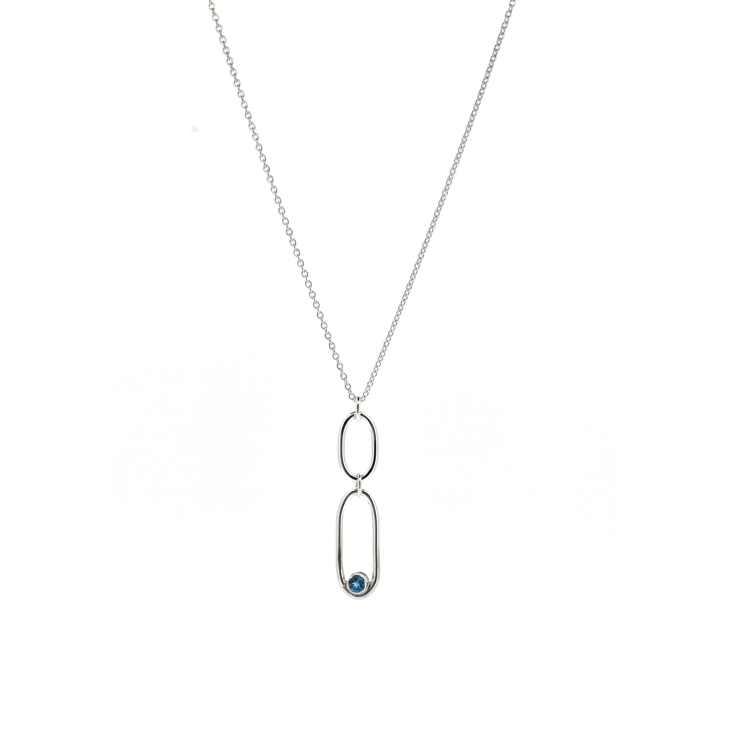 A silver pendant featuring 2 open oblong shaped of different sizes with a blue topaz gemstone set inside one curve. On a silver chain.