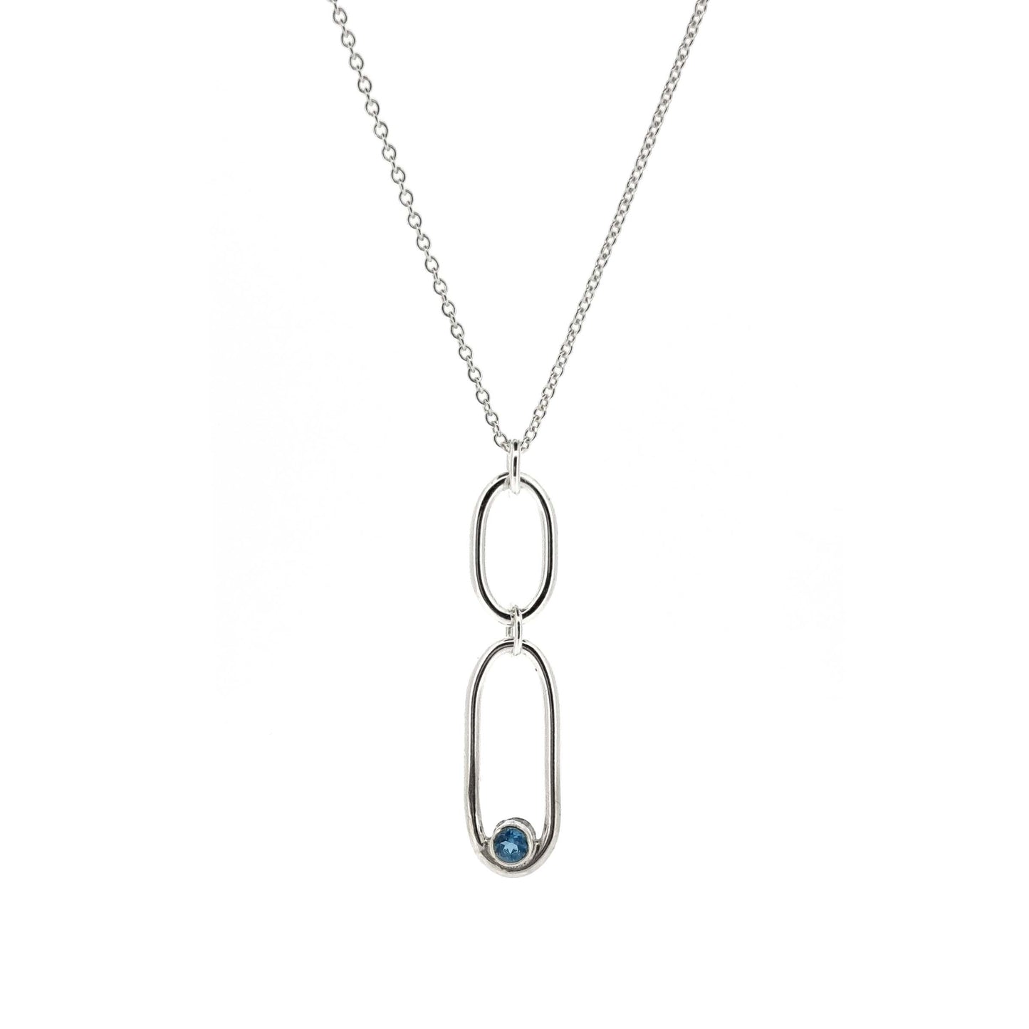A silver pendant featuring 2 open oblong shaped of different sizes with a blue topaz gemstone set inside one curve. On a silver chain.