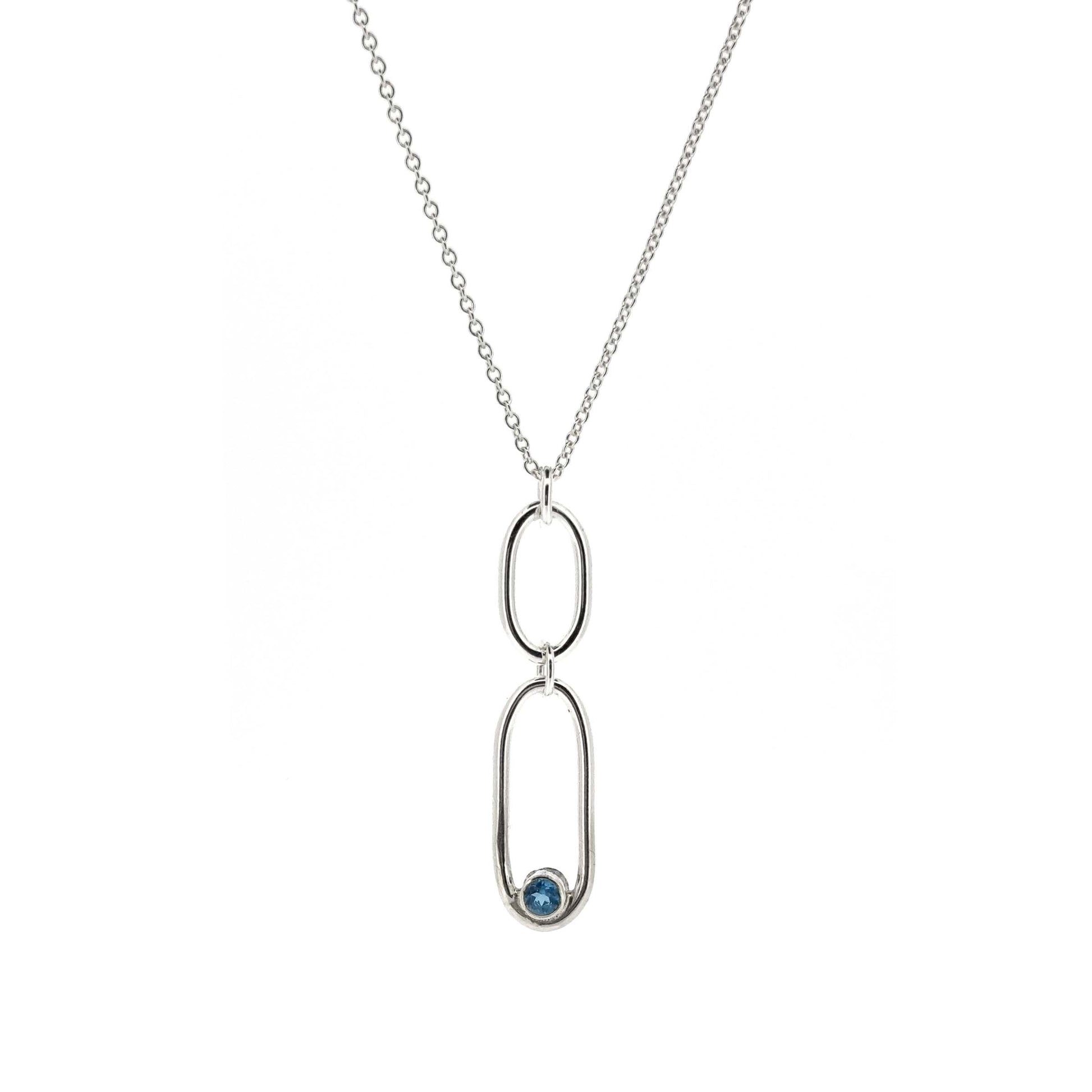 A silver pendant featuring 2 open oblong shaped of different sizes with a blue topaz gemstone set inside one curve. On a silver chain.