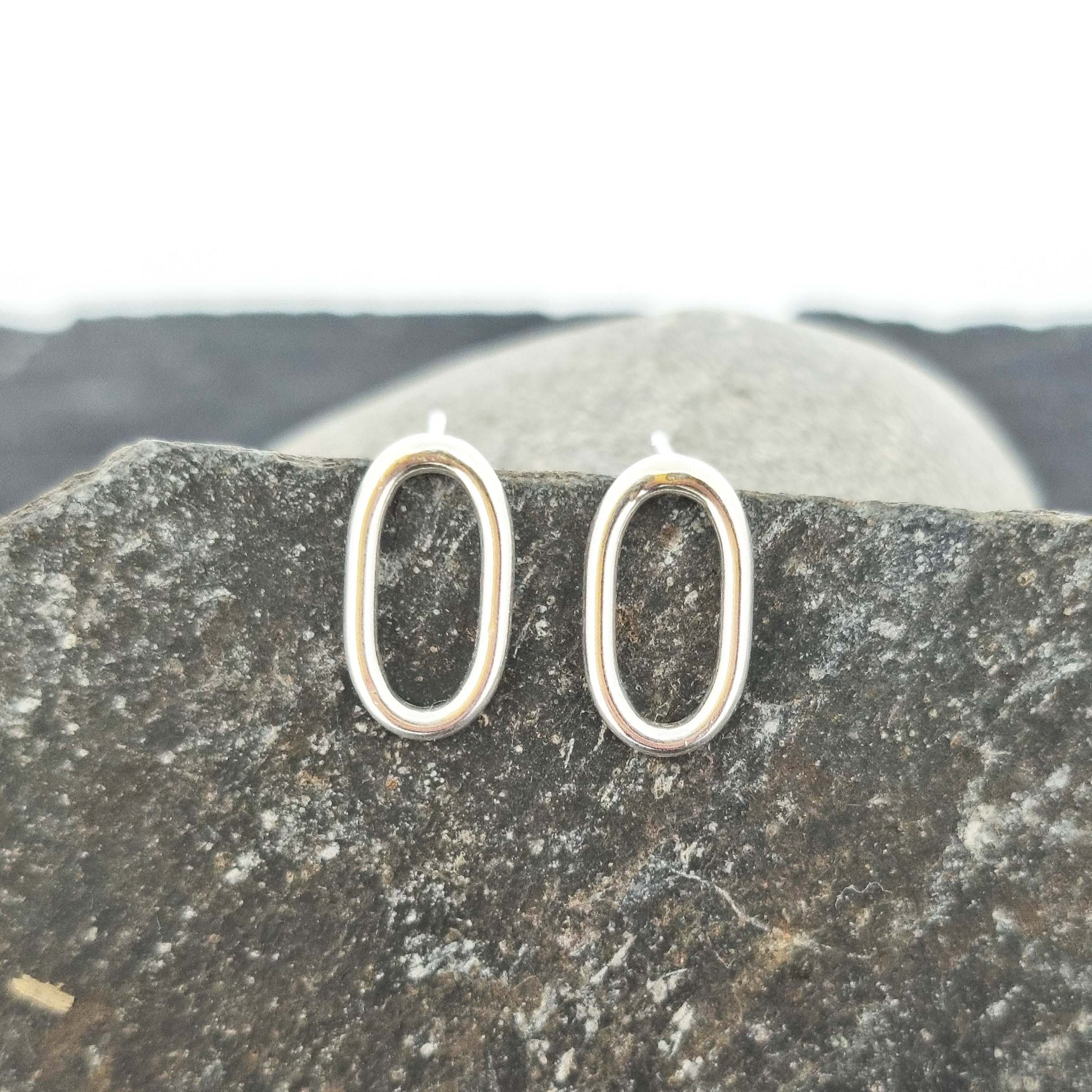 Silver open oblong stud earrings. Pictured on stones.