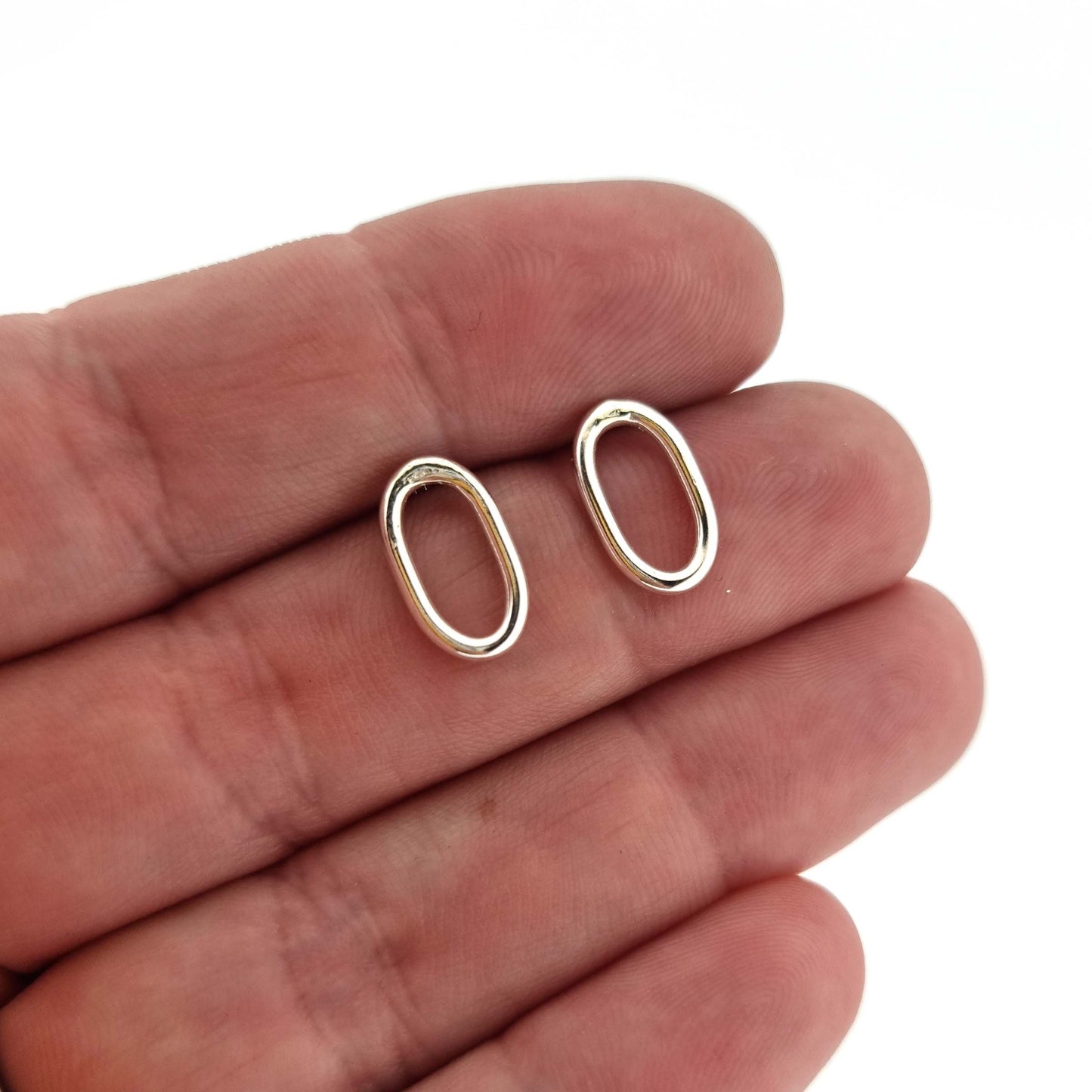 Silver open oblong stud earrings. Pictured in a hand.