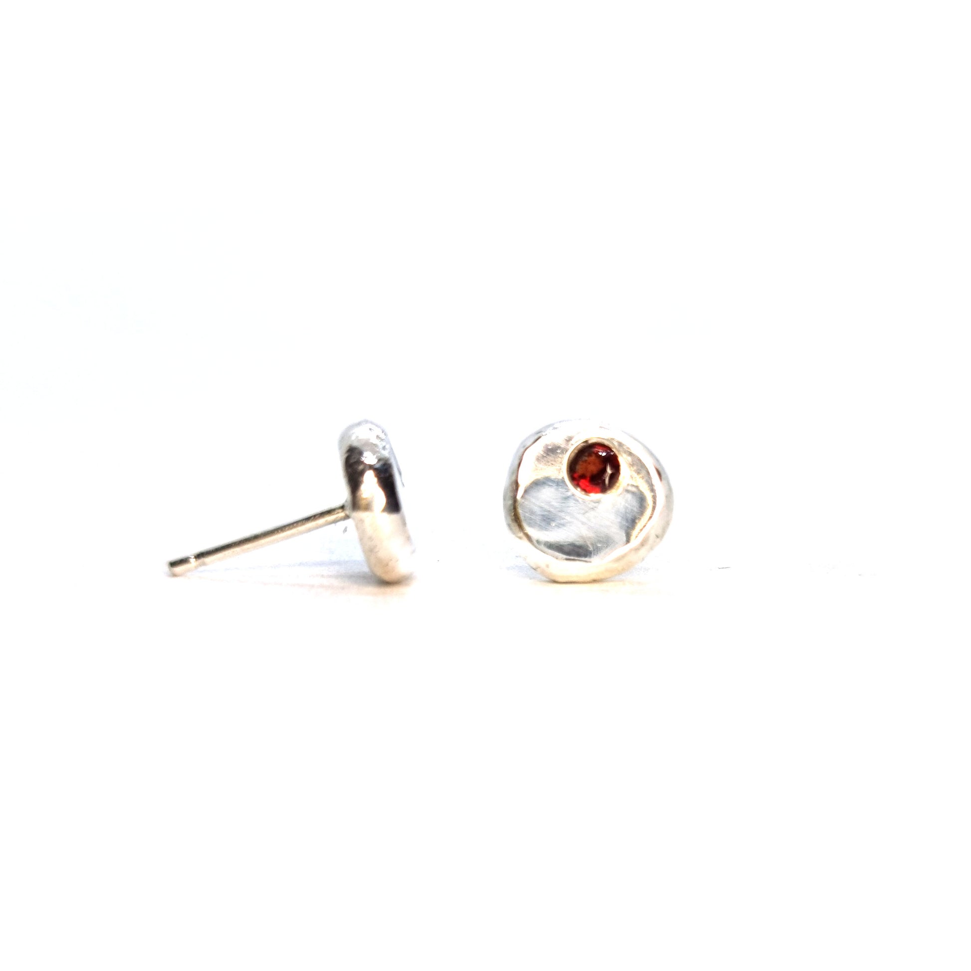 Round silver stud earrings with red garnet gemstones set off-centre.