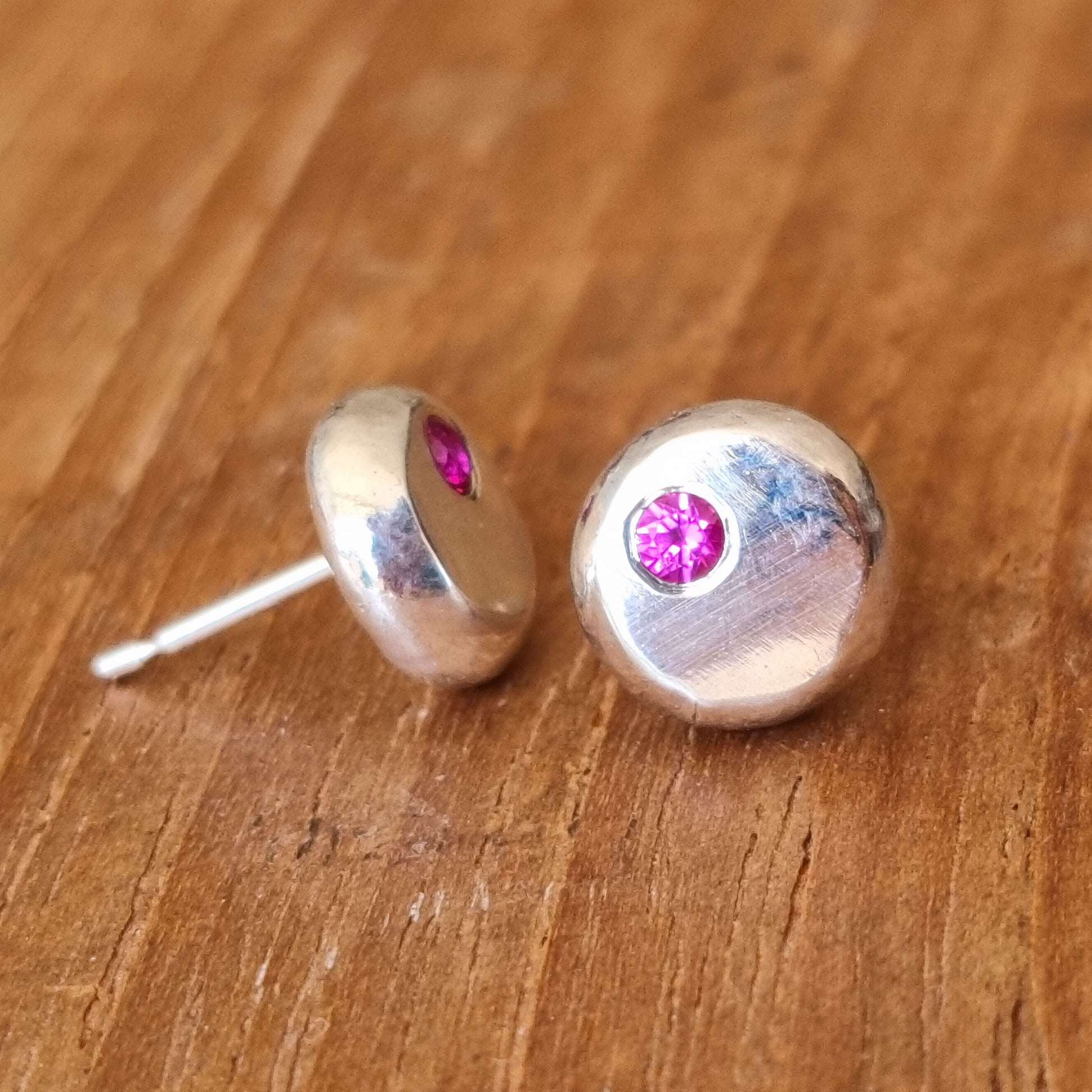 Round silver pebble stud earrings with red rubies flush set off-centre.