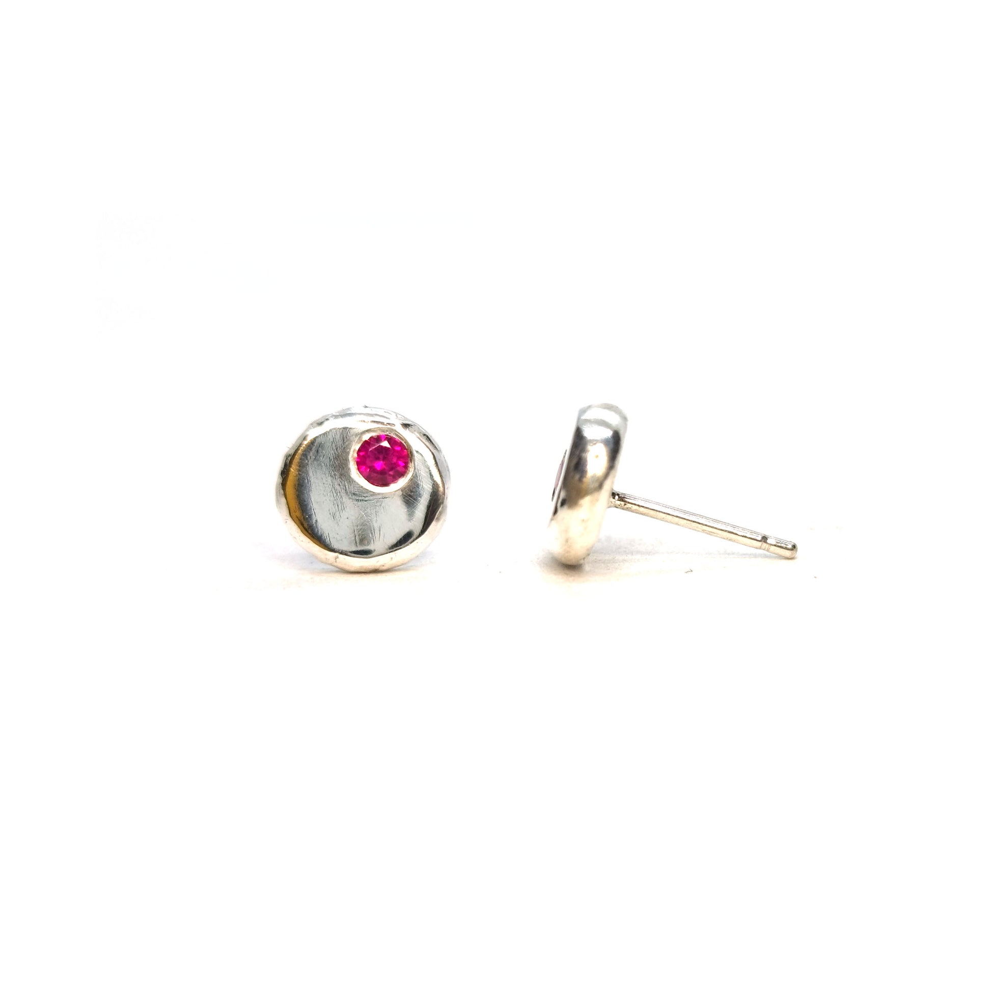 Round silver pebble stud earrings with red rubies flush set off-centre.