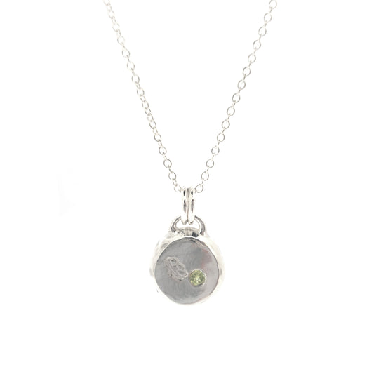 Silver round flat 'pebble' birthstone pendant with a poppy engraved on it and a pale green peridot gemstone on a silver chain. - August