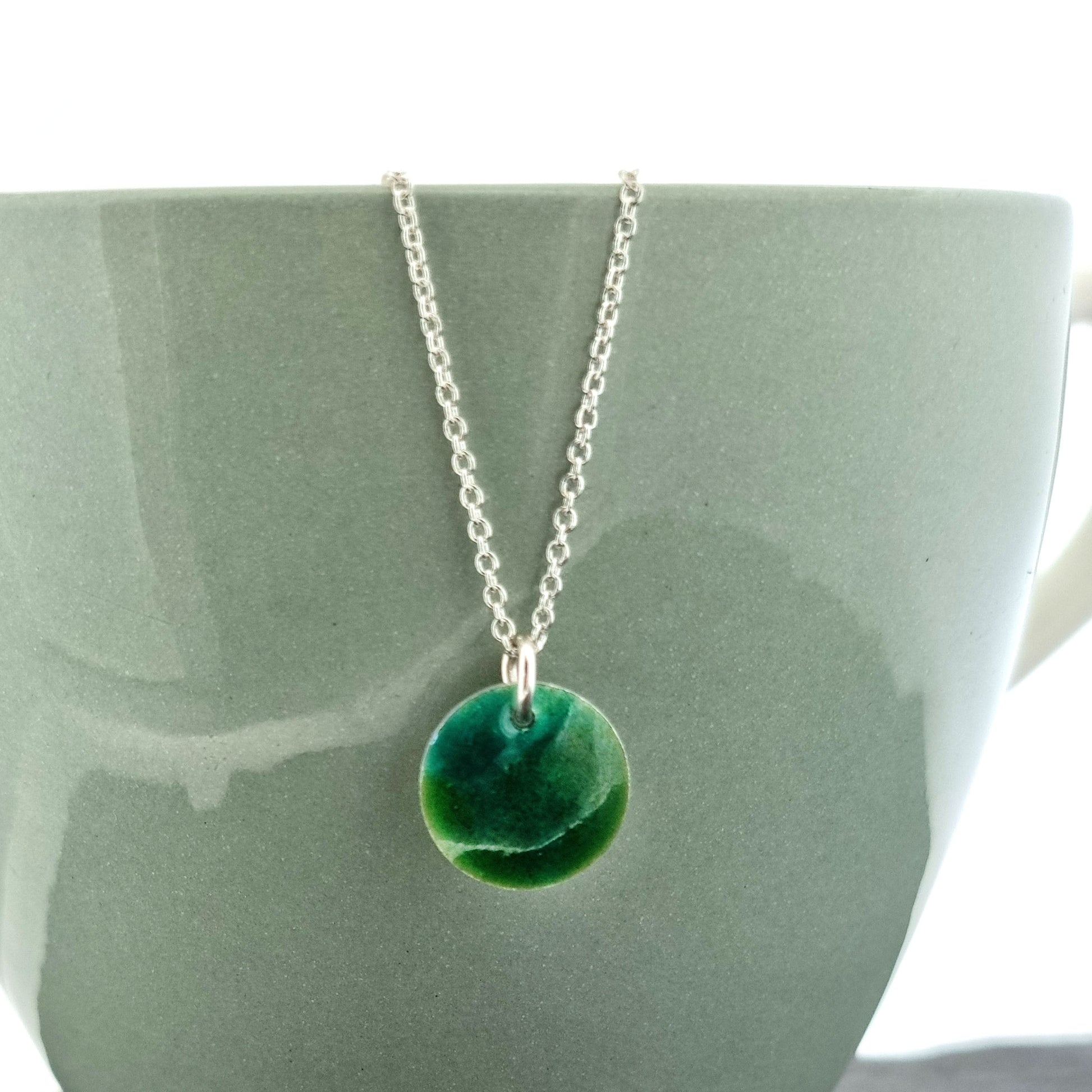 A round silver pendant with a mix of green enamels. On a silver chain.