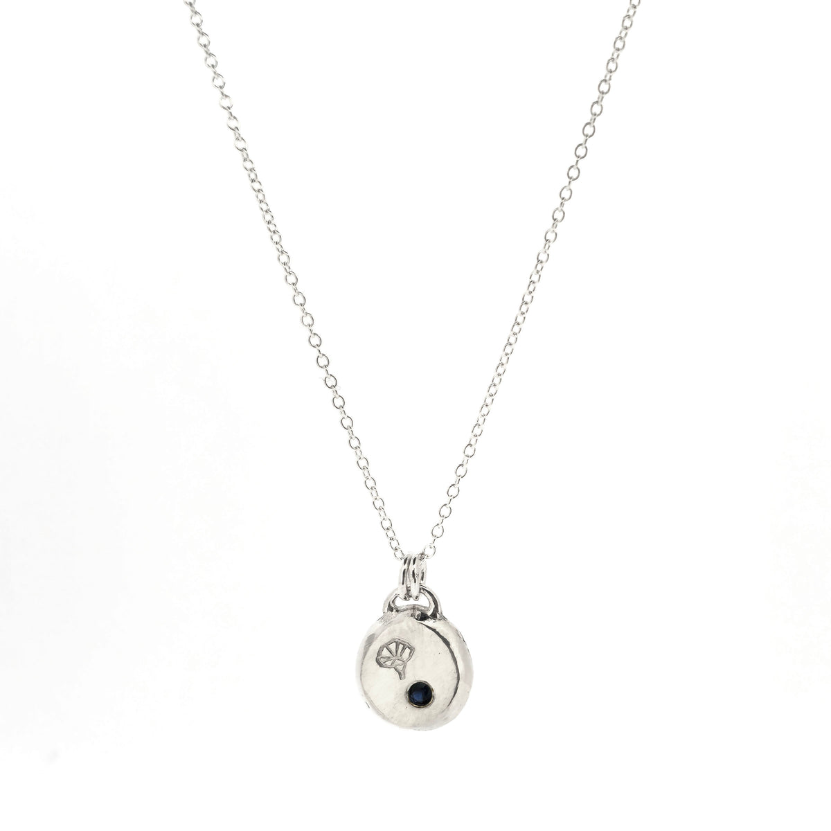 A handmade silver pebble pendant necklace featuring a disc-shaped charm with a small dark blue gemstone and an engraved morning glory flower design, suspended from a delicate silver chain against a white background. Mijoux Jewellery.
