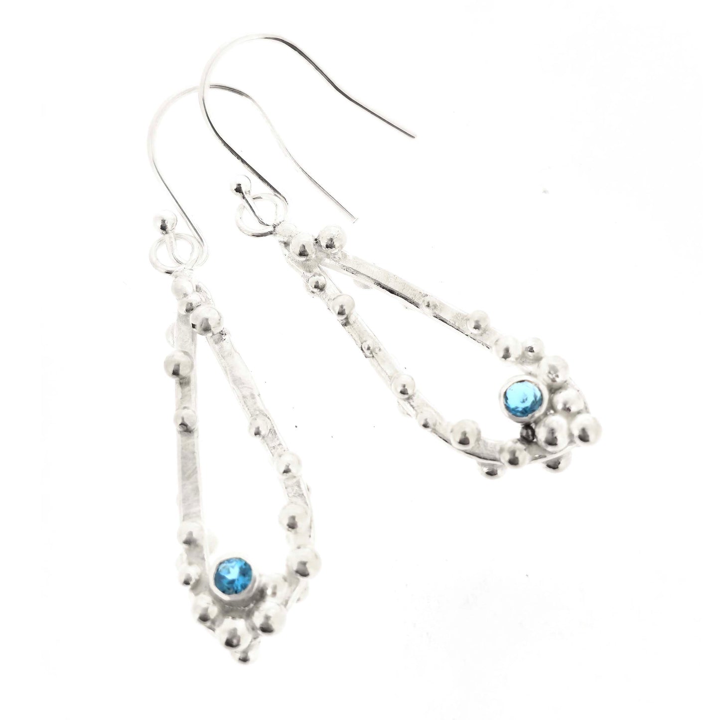 Silver drop earrings with open asymmetrical teardrop shape and silver balls and round blue gemstones. On a white background.