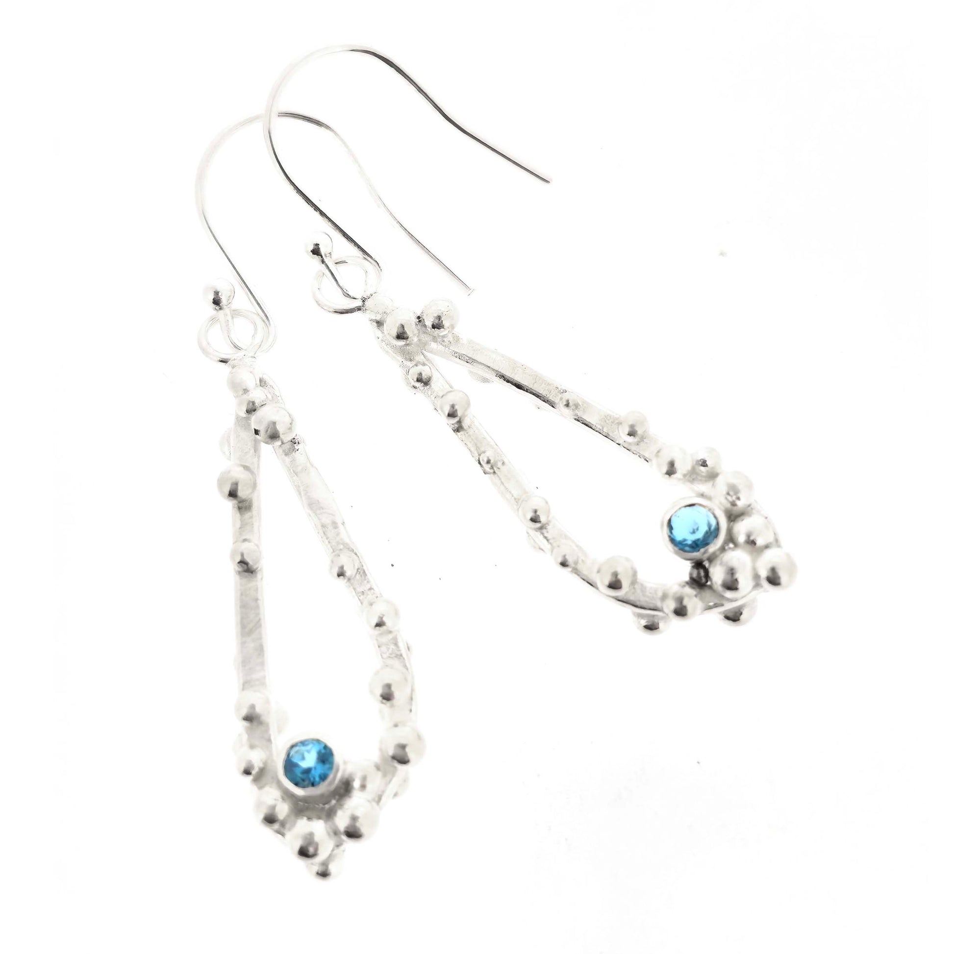 Silver drop earrings with open asymmetrical teardrop shape and silver balls and round blue gemstones. On a white background.
