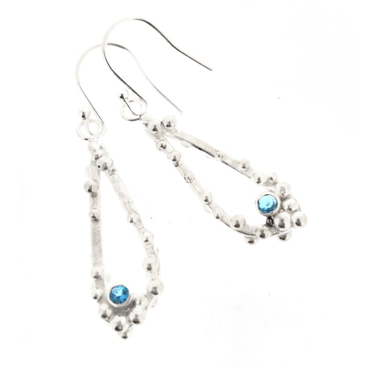 Silver drop earrings with open asymmetrical teardrop shape and silver balls and round blue gemstones. On a white background.