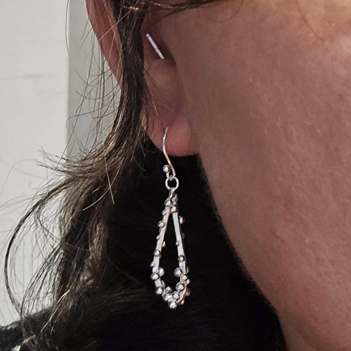 Silver drop earrings in a asymmetrical open teardrop shape with silver balls. Shown being worn.