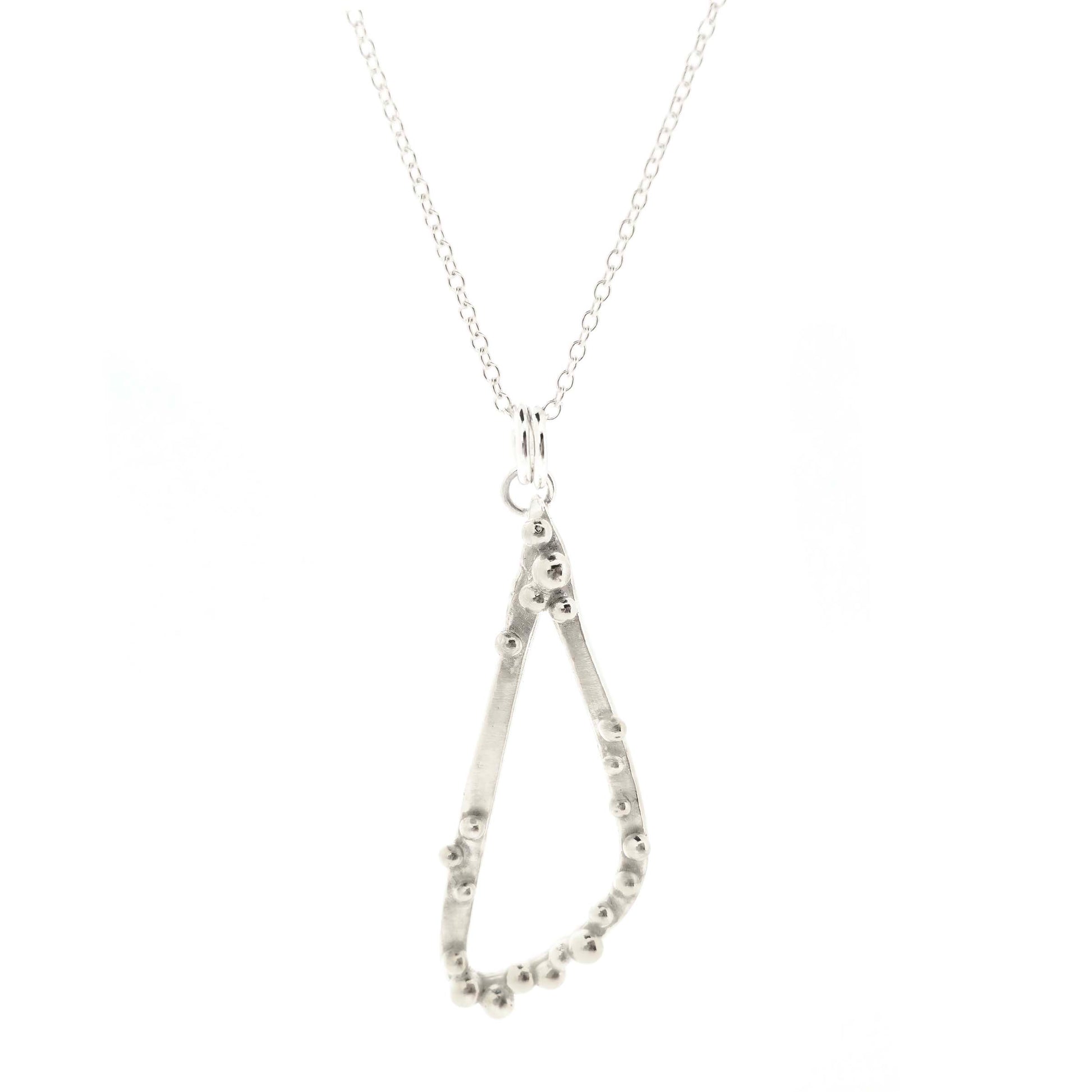 A silver asymmetrical pendant with a soft open triangle shape and silver balls, suspended from a silver chain. Shown on a white backgound. 