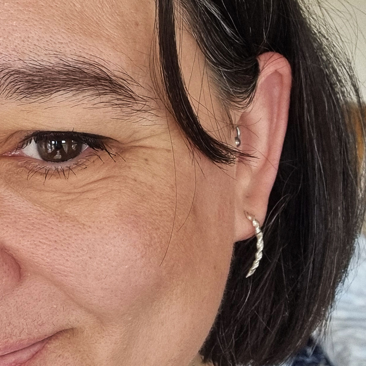 Silver twist curved drop earrings with post fitting. Shown being worn on ear lobe.
