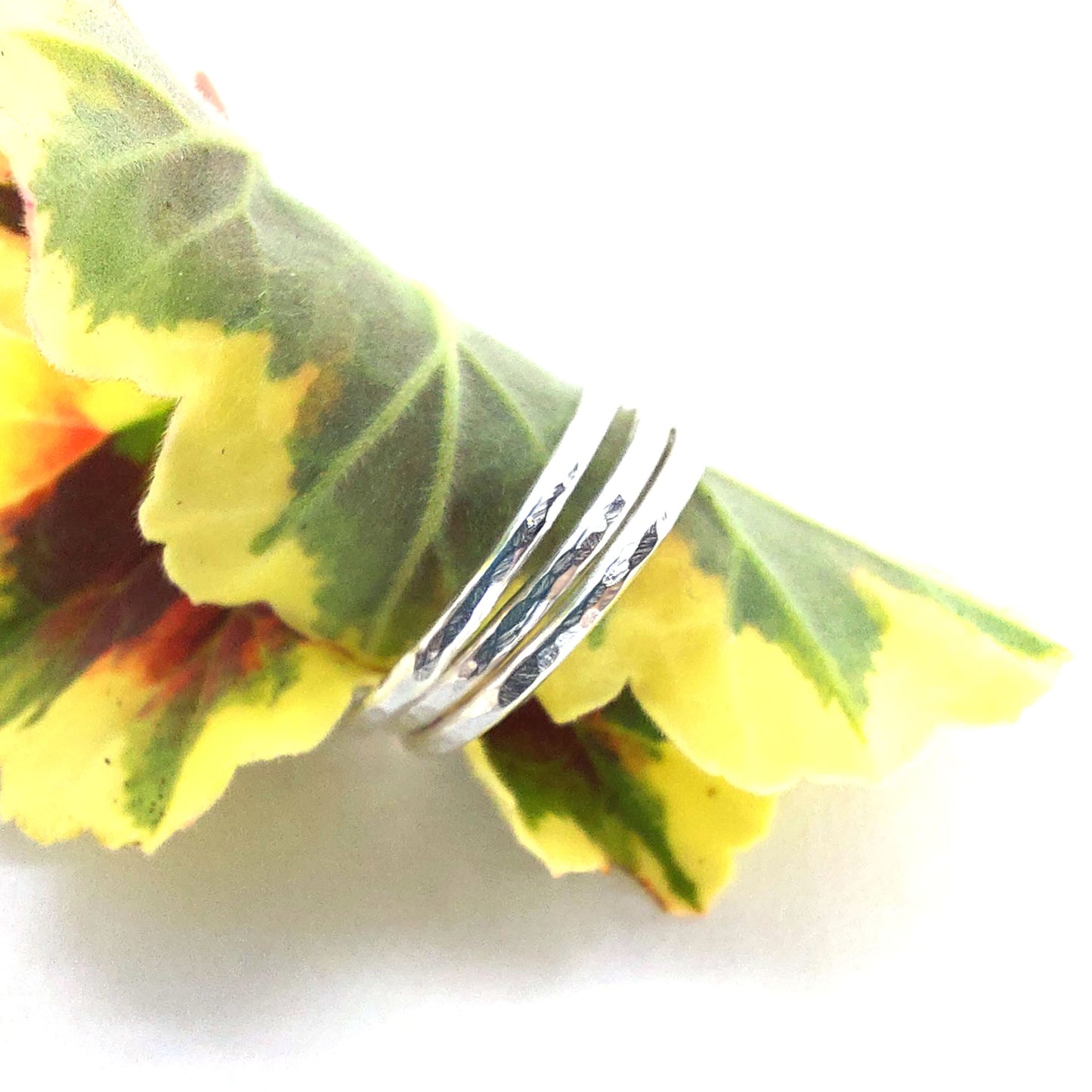A set of 3 thin silver stacking rings with a hammered finish. Shown pictured on a leaf.