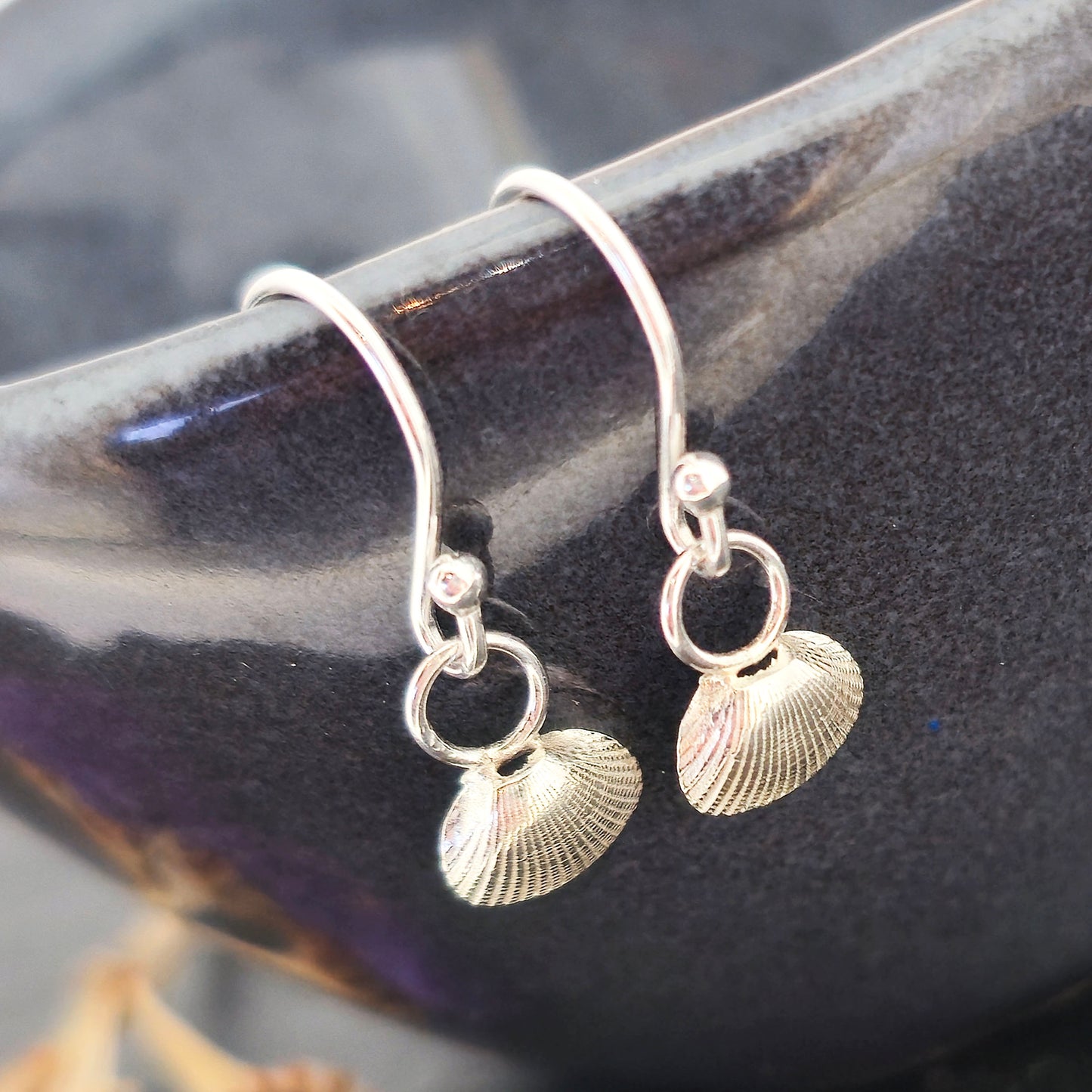 Silver cockle shell drop earrings on black bowl. Handmade. Mijoux Jewellery.