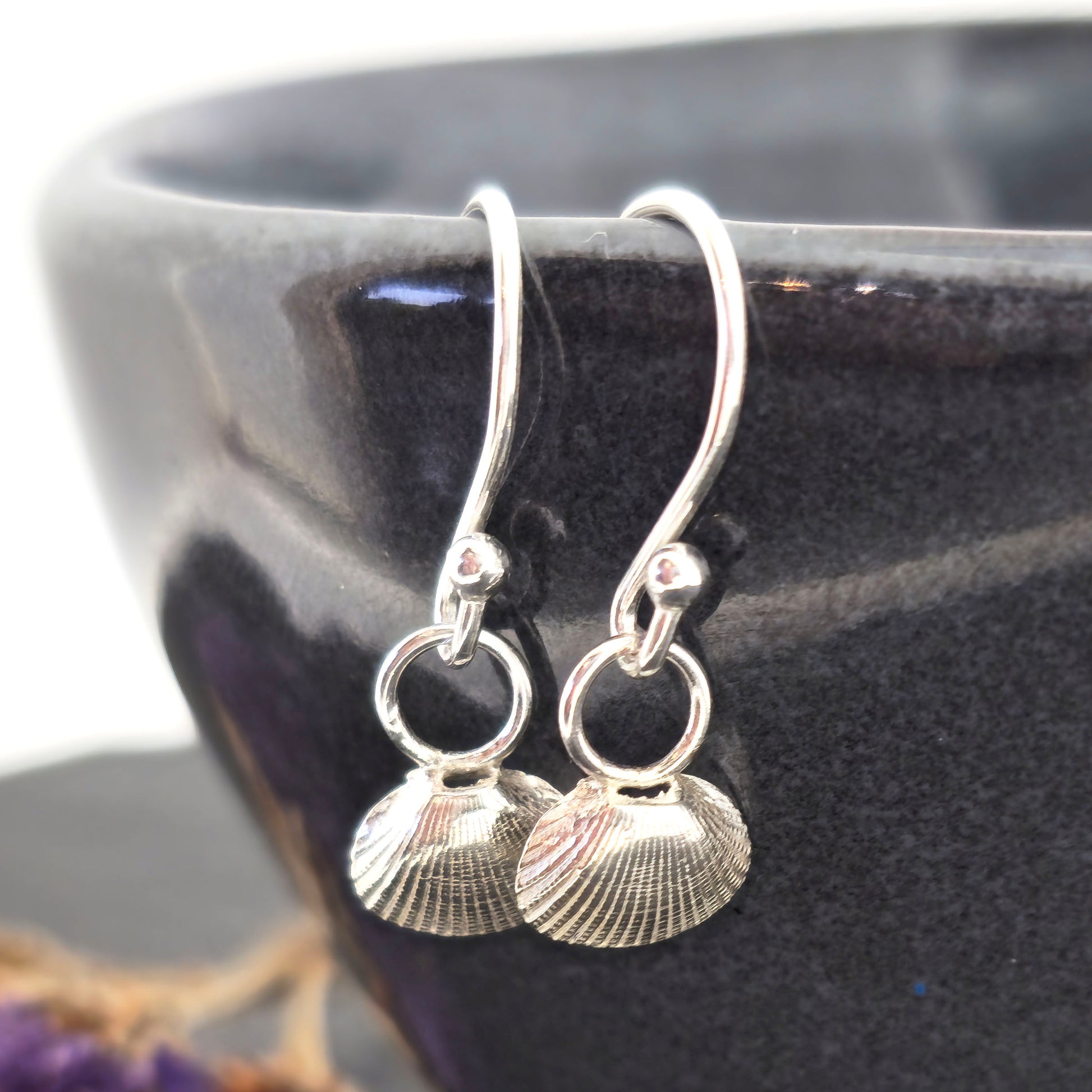 Silver cockle shell drop earrings on black bowl. Handmade. Mijoux Jewellery.