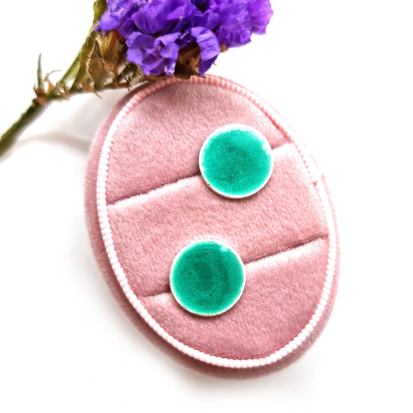 Round silver stud earrings with light green enamel. Pictured in a jewellery box with flowers.