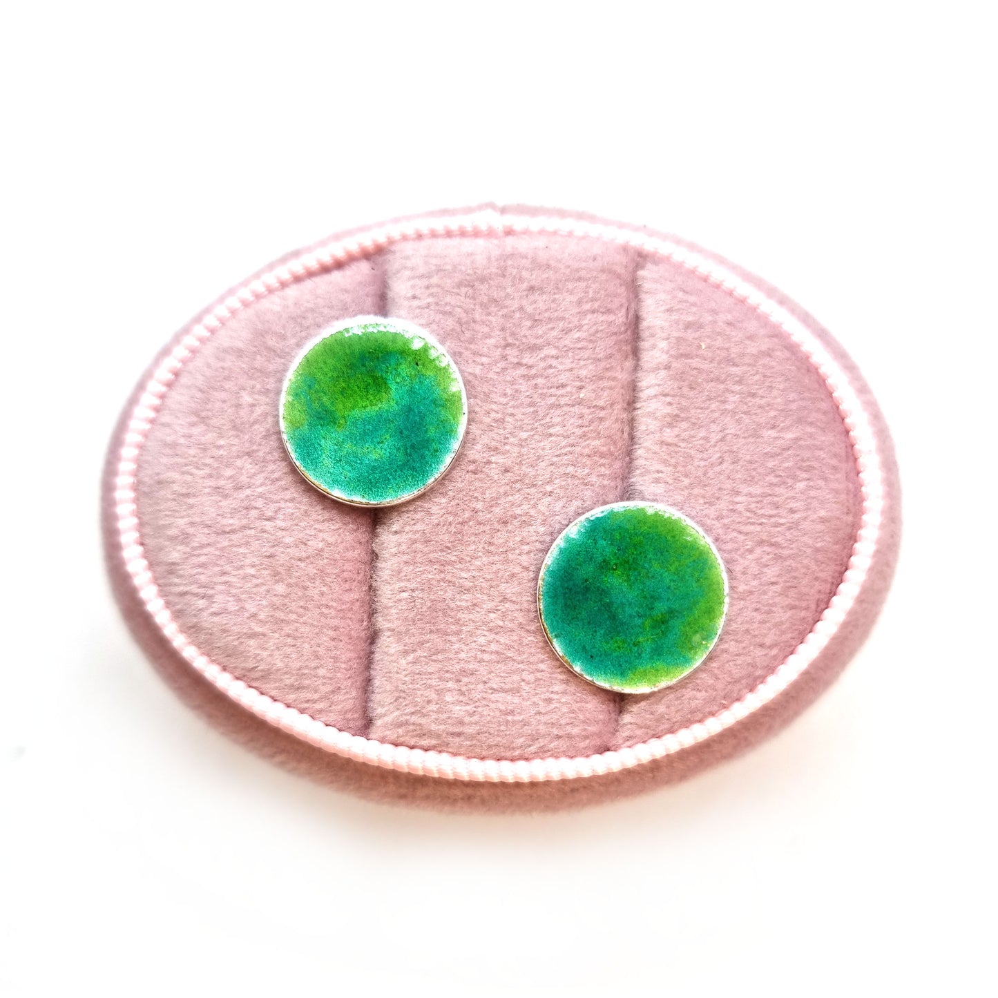 Round silver stud earrings with a mix of green enamels. Pictured in a jewellery box.