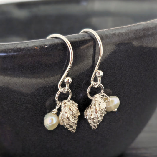 A pair of silver periwinkle shell and freshwater pearl drop earrings on a black bowl. Handmade. Mijoux Jewellery.