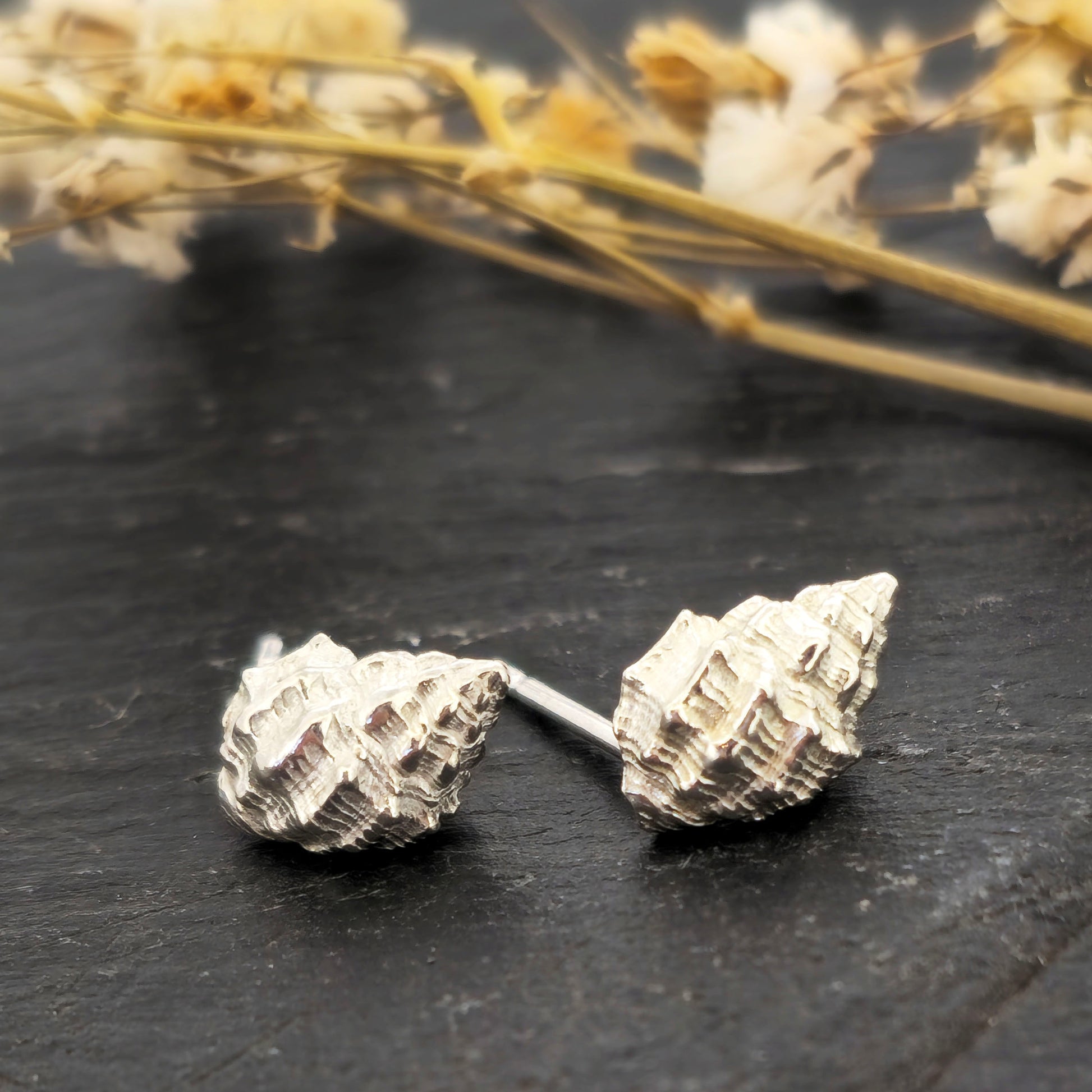 Silver Periwinkle shell stud earrings on a black background with flowers. Handmade. Mijoux Jewellery.