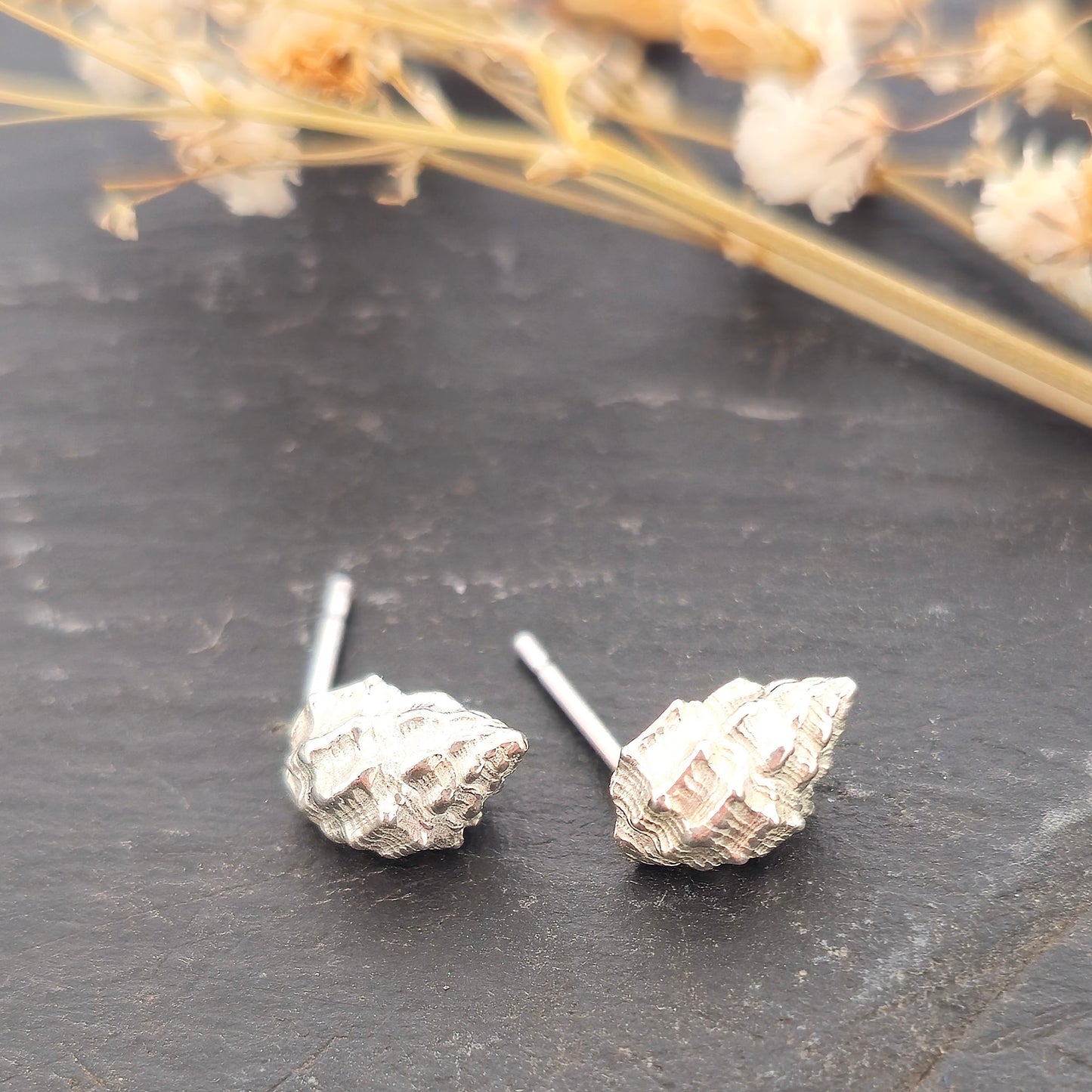 Silver Periwinkle shell stud earrings on a black background with flowers. Handmade. Mijoux Jewellery.
