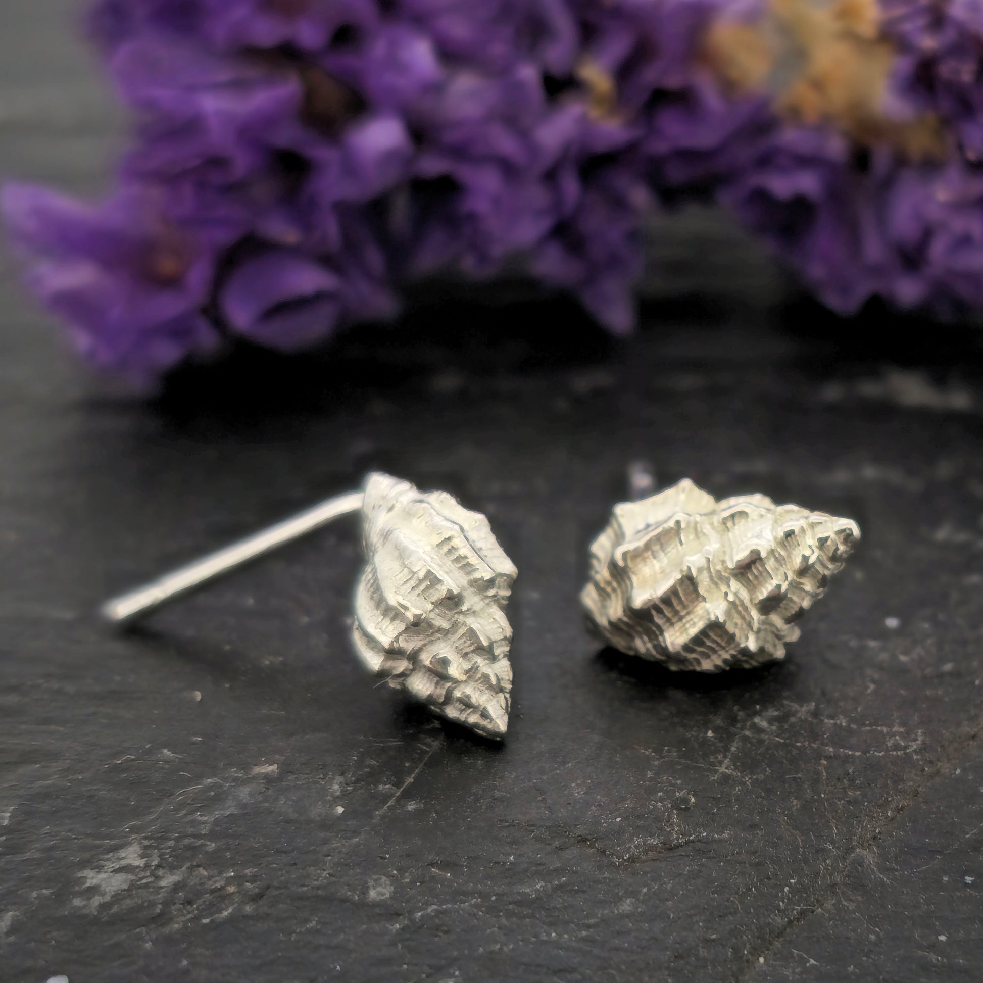 Silver Periwinkle shell stud earrings on a black background with flowers. Handmade. Mijoux Jewellery.