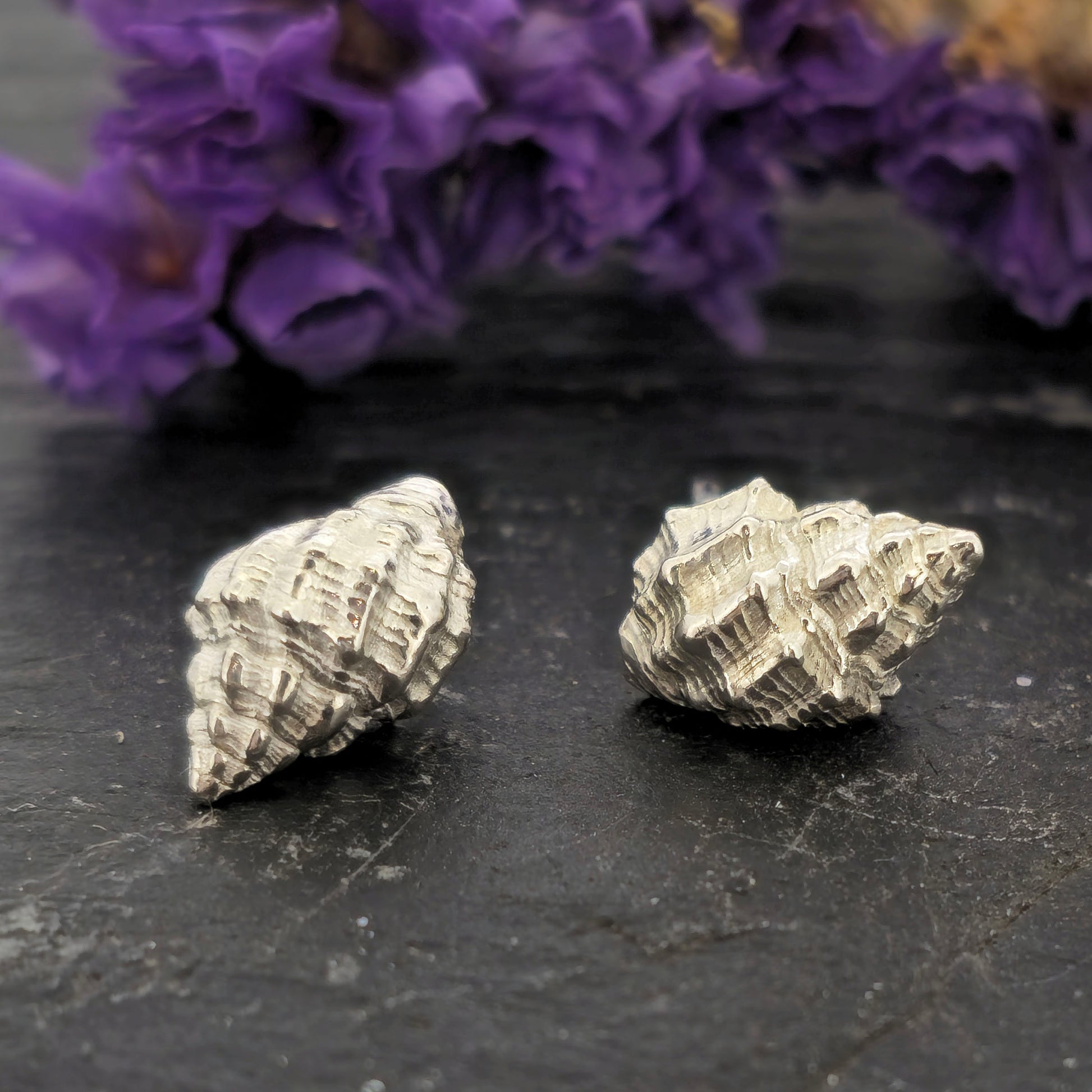 Silver Periwinkle shell stud earrings on a black background with purple flowers. Handmade. Mijoux Jewellery.