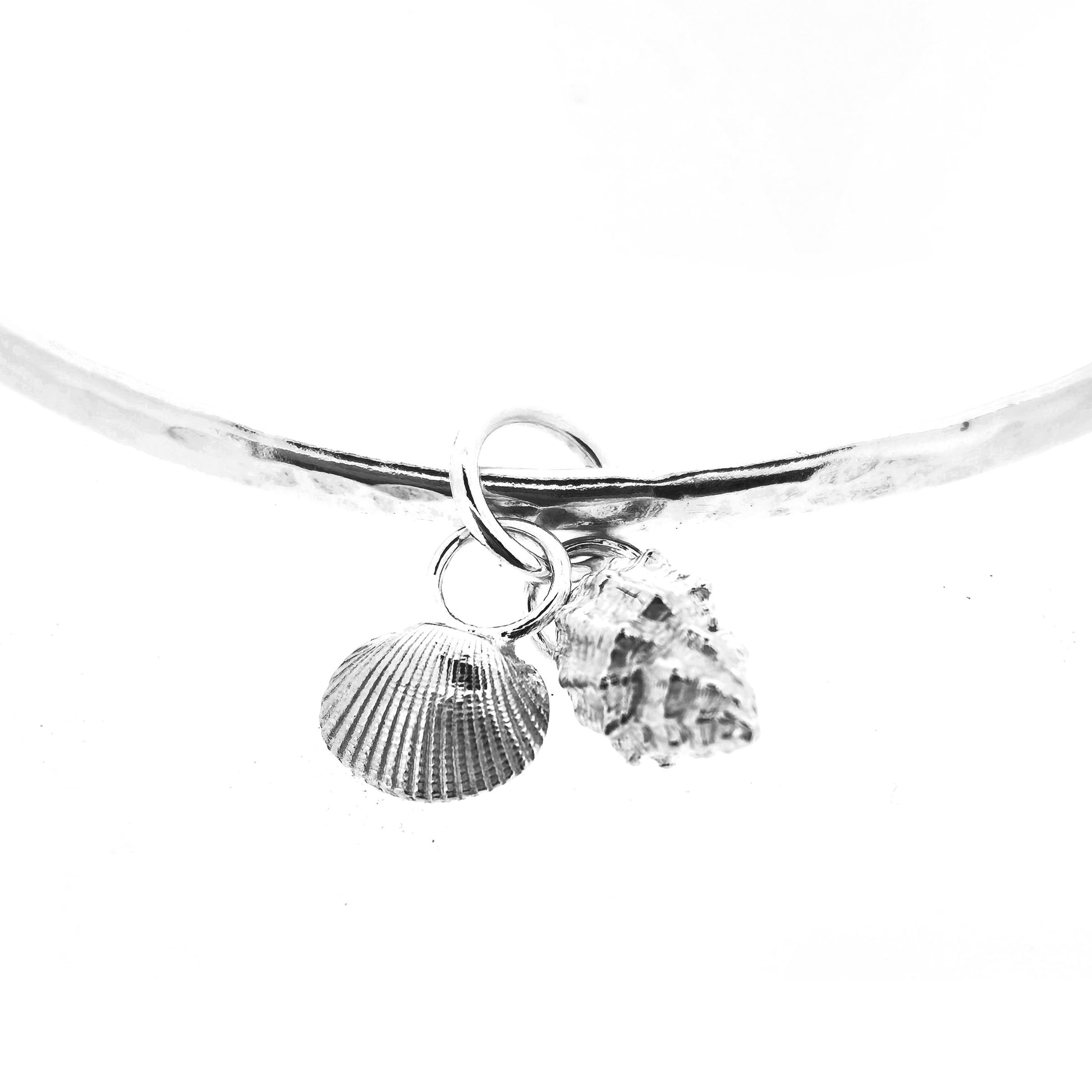 A close up of two shell charms on a bangle. 1 cockle shell and 1 periwinkle shell. On a white background. Handmade. Mijoux Jewellery.