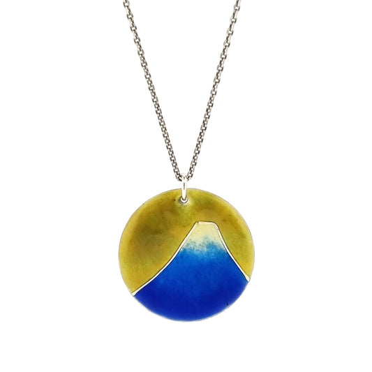 Round silver pendant with a mountain on in graduated blue enamel and a white top and a yellow enamel background. Suspended from a silver chain.