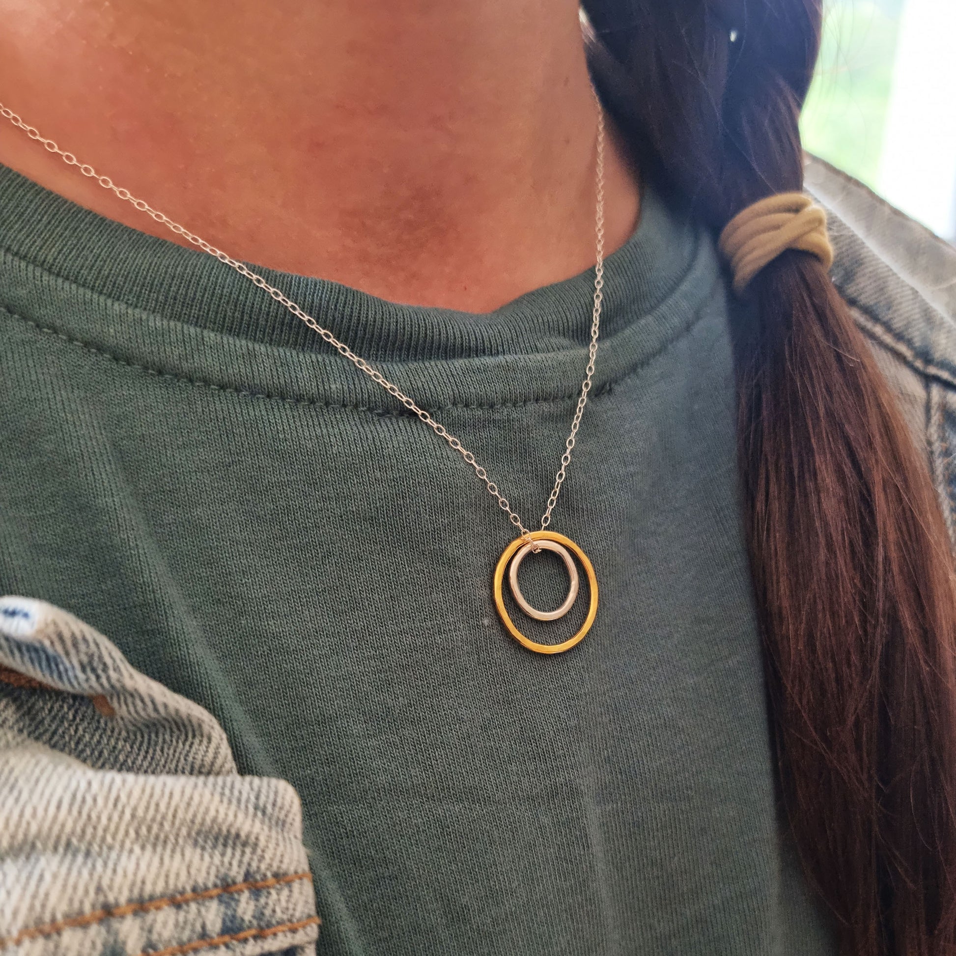 A double circle pendant with an inner silver hammered circle and an outer yellow gold vermeil hammered circle. Suspended on a silver chain. Pictured being worn.