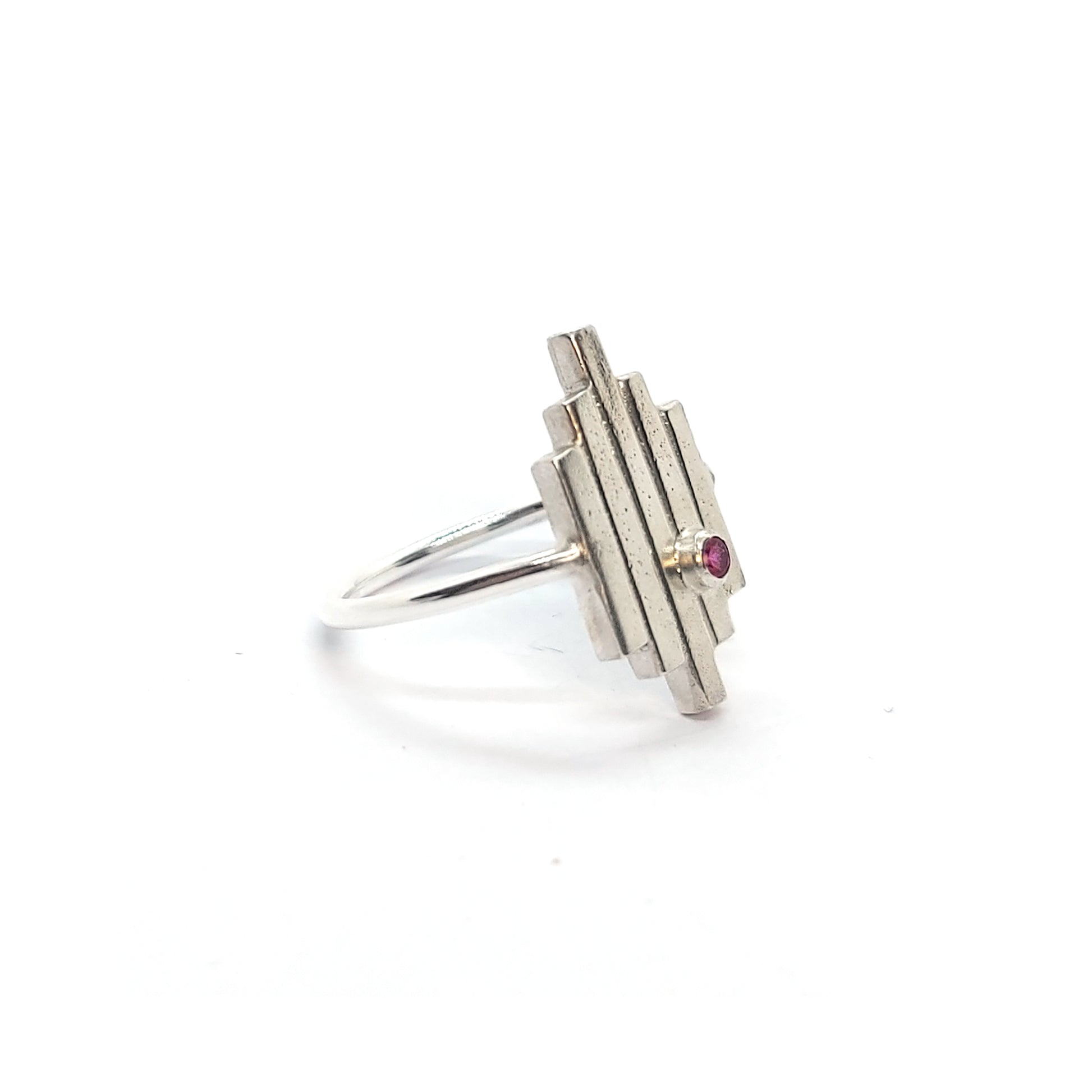 An Art Deco style silver ring with 5 straight lines and an off-centre pinky red ruby