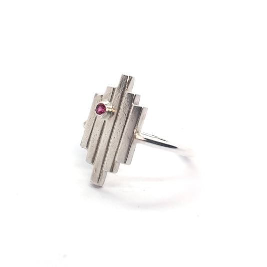 An Art Deco style silver ring with 5 straight lines and an off-centre pinky red ruby