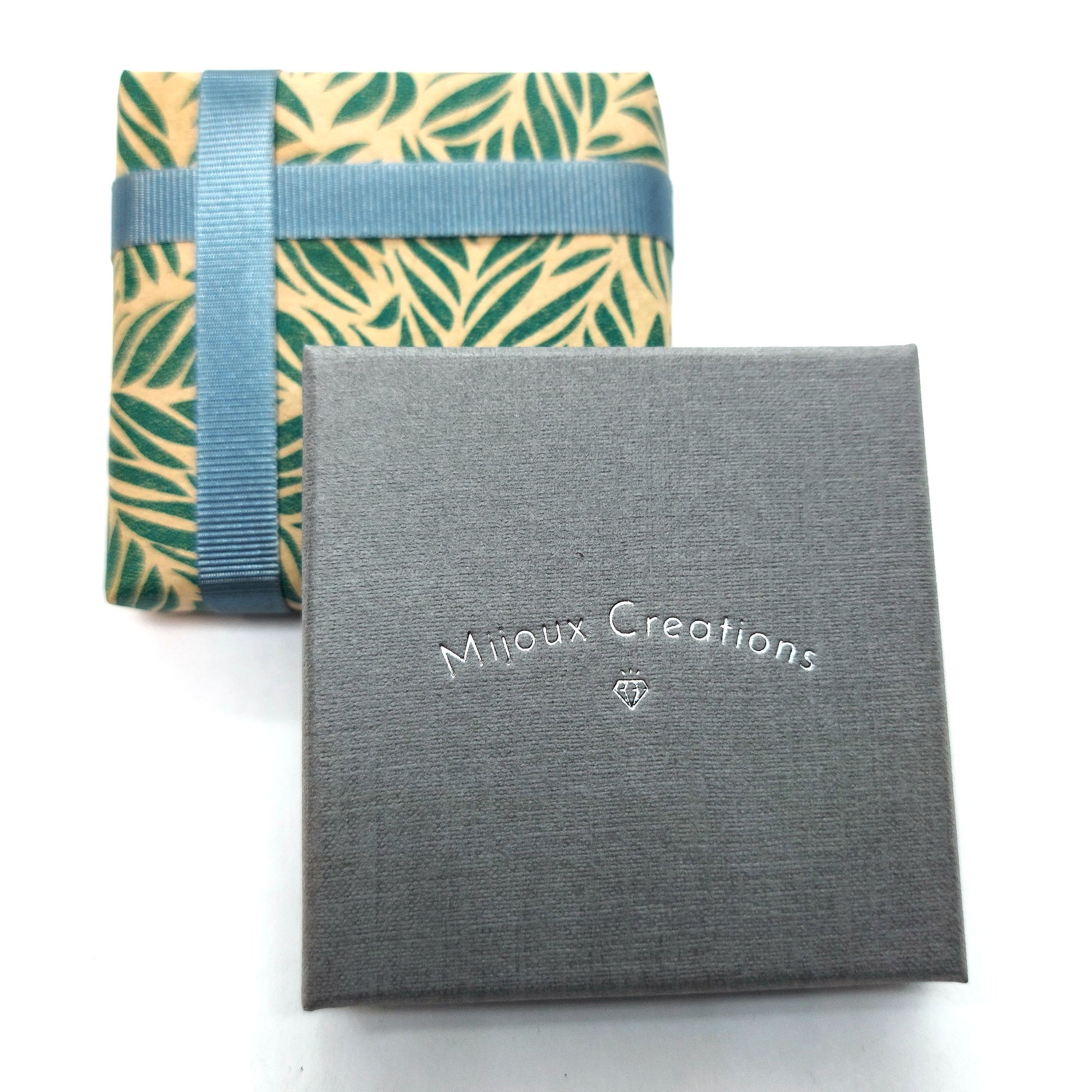 A wrapped box with leaf pattern brown and green wrapping paper and grey ribbon alongside a grey Mijoux Creations gift box.