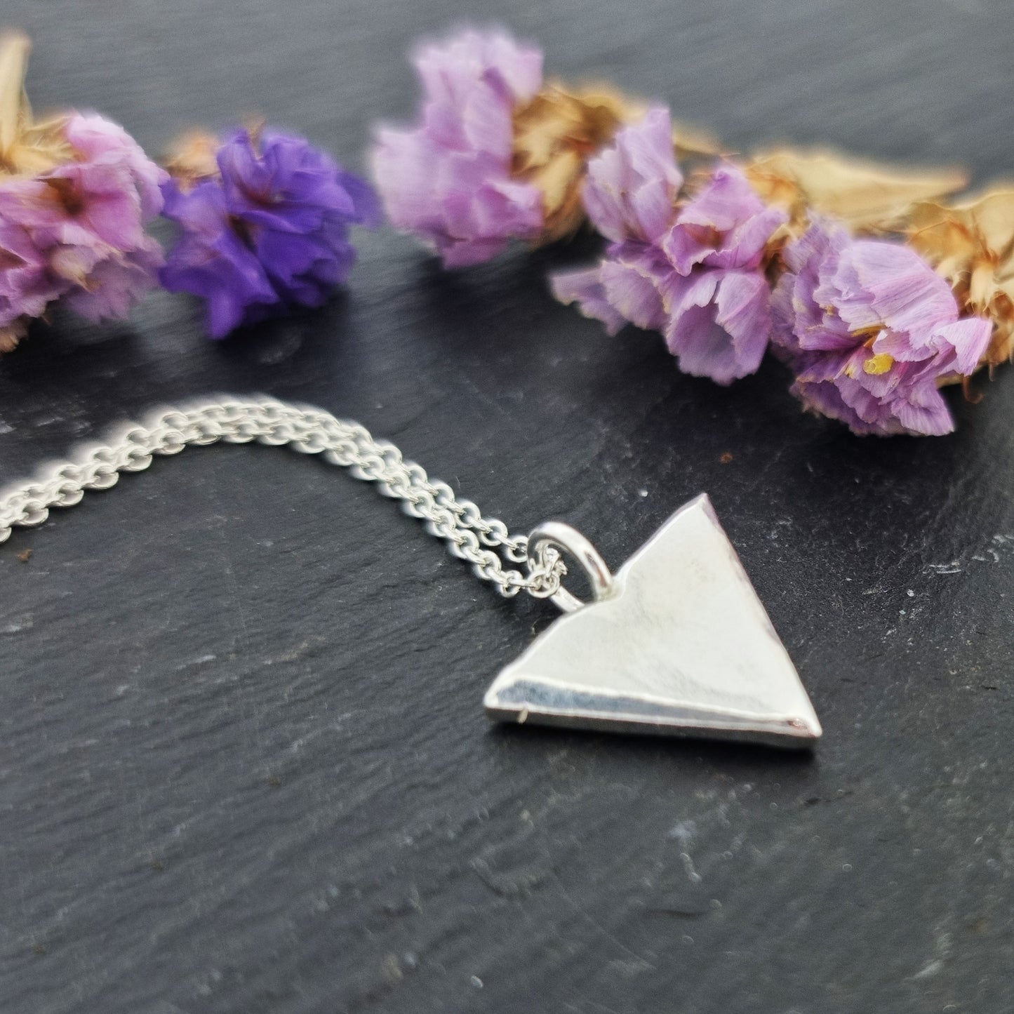 A silver beveled triangle shaped pendant on a silver chain. With flowers