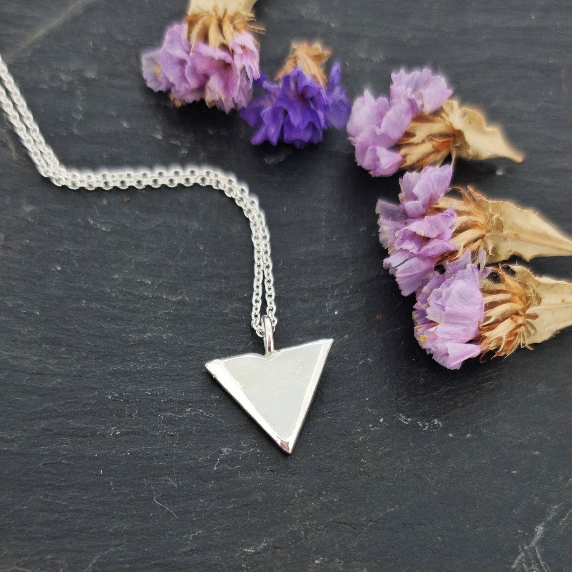 A silver beveled triangle shaped pendant on a silver chain. With flowers