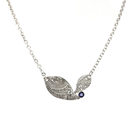 An asymmetric silver necklace with a patterned focal point set with a blue/purple gemstone