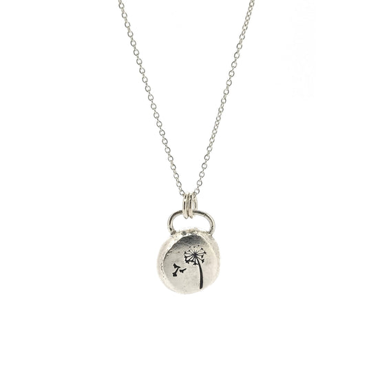 A silver organic round flat pebble pendant with dandelion and fluff engraved on it. On a silver chain,