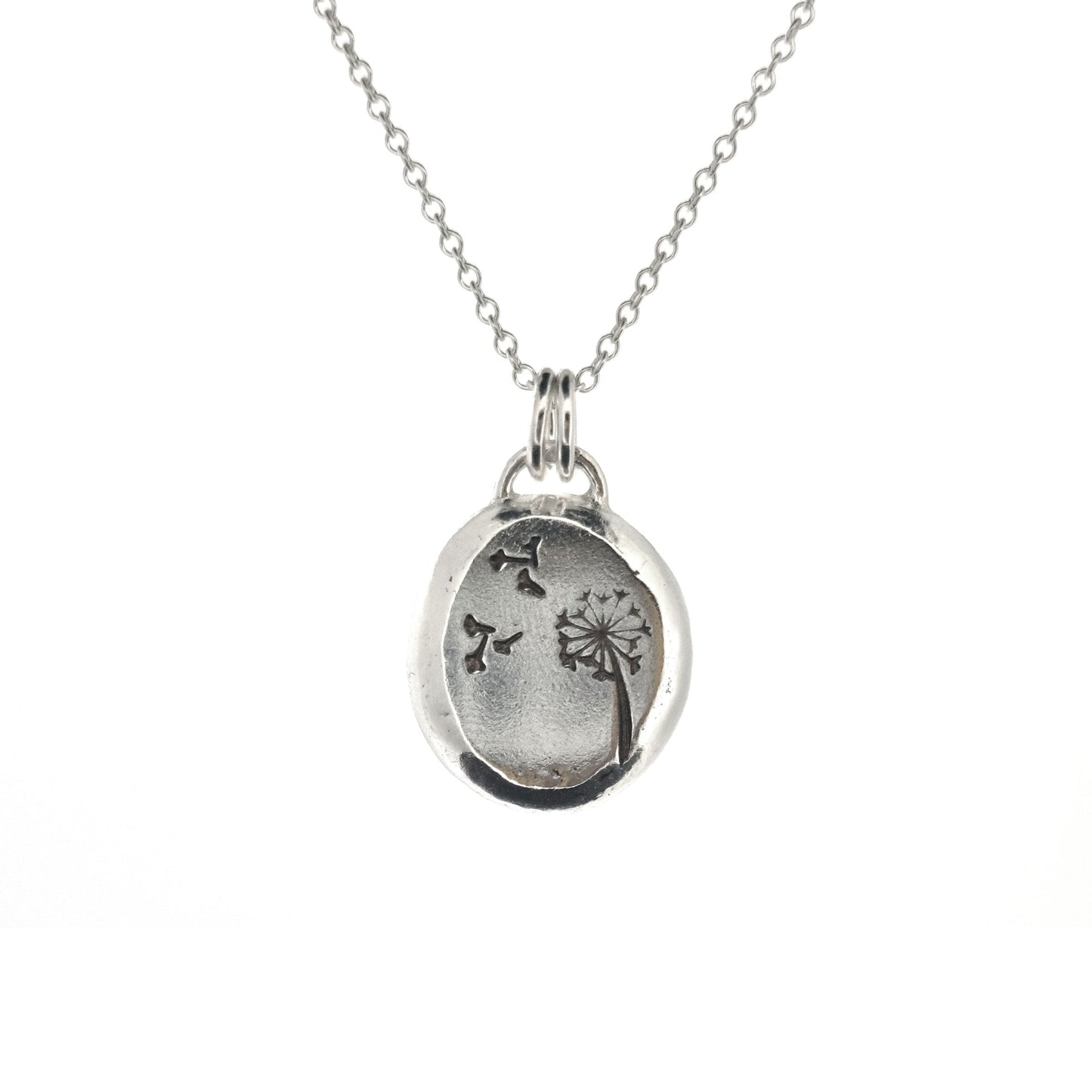 A silver organic round flat pebble pendant with dandelion and fluff engraved on it. On a silver chain.