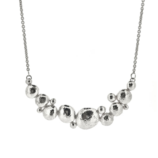 A silver necklace with a curve made up of silver balls of various sizes and with a chain necklace.