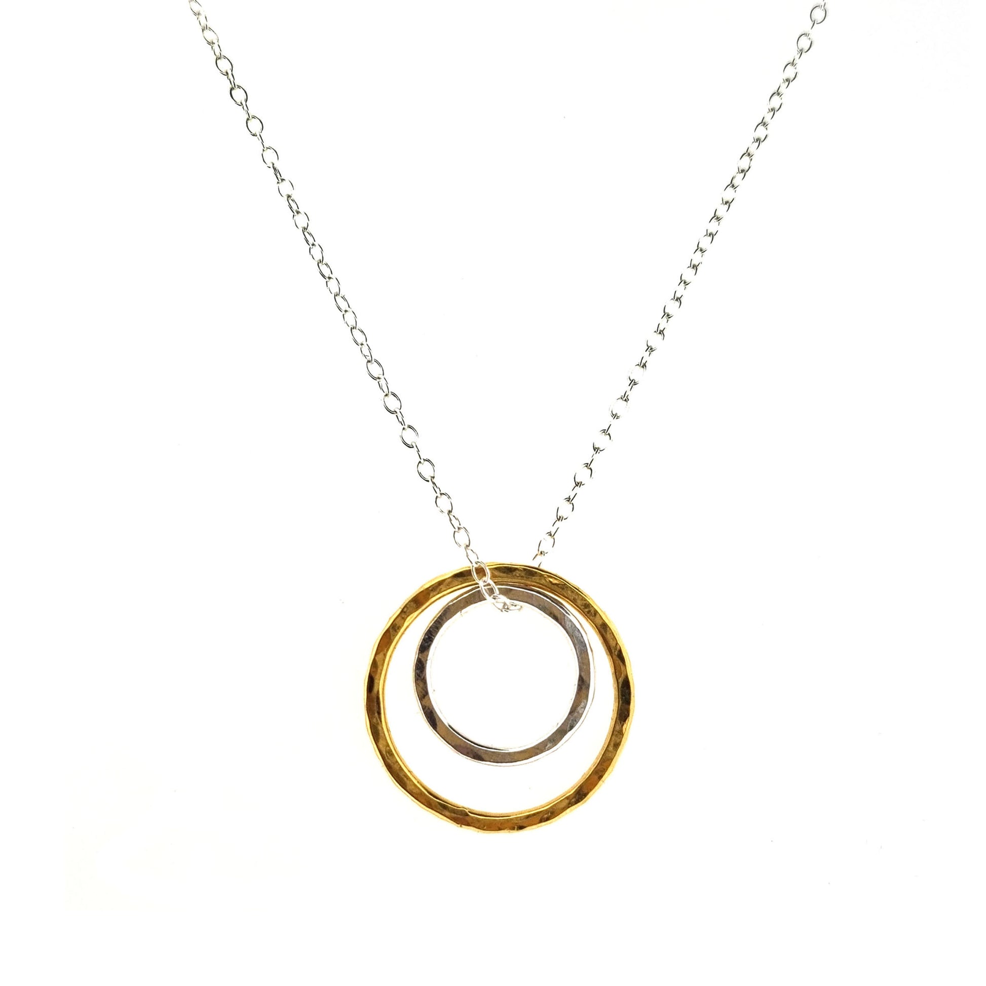 A double circle pendant with an inner silver hammered circle and an outer yellow gold vermeil hammered circle. Suspended on a silver chain.