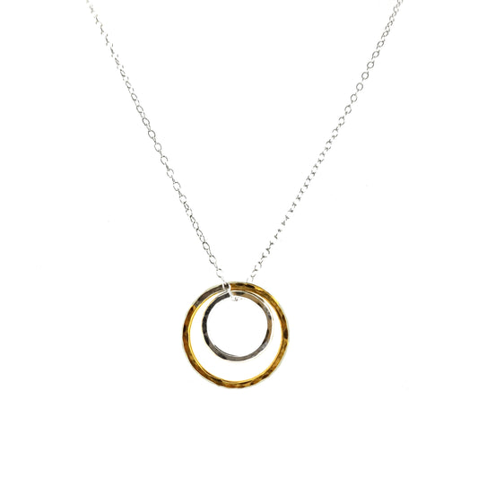 A double circle pendant with an inner silver hammered circle and an outer yellow gold vermeil hammered circle. Suspended on a silver chain.