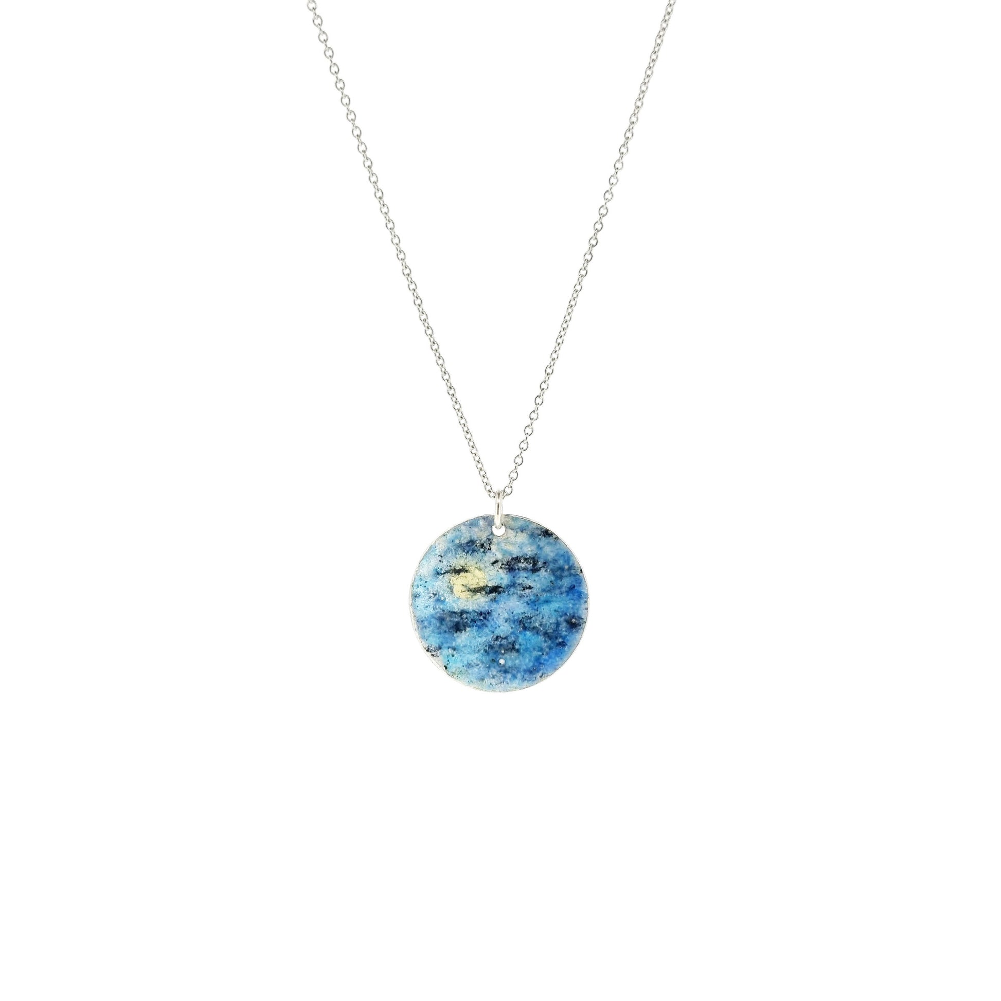 A round silver pendant with a night sky scene painted in blue, black and white enamels. On a silver chain.