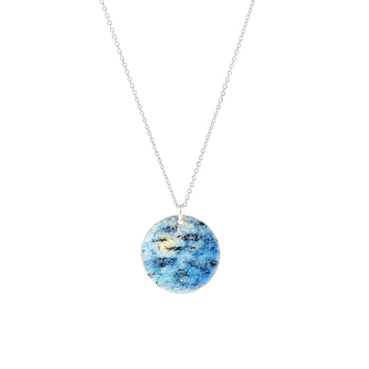 A round silver pendant with a night sky scene painted in blue, black and white enamels. On a silver chain.