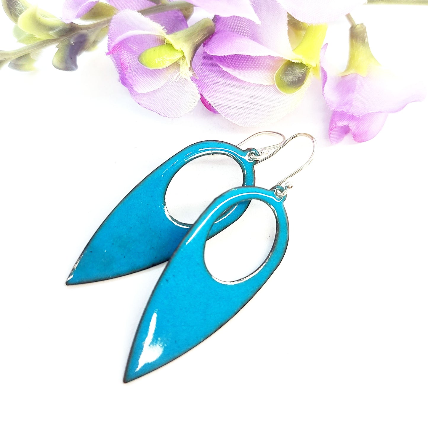 Teardrop shaped drop earrings with a circle cut our covered in teal enamel. On silver ear hooks. Pictured with flowers