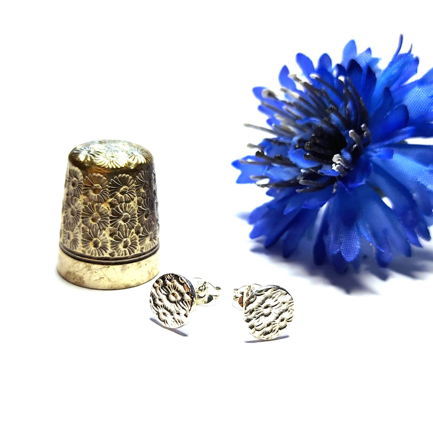 Round silver stud earrings with a pattern of flowers. Pictured with a thimble and blue flower.