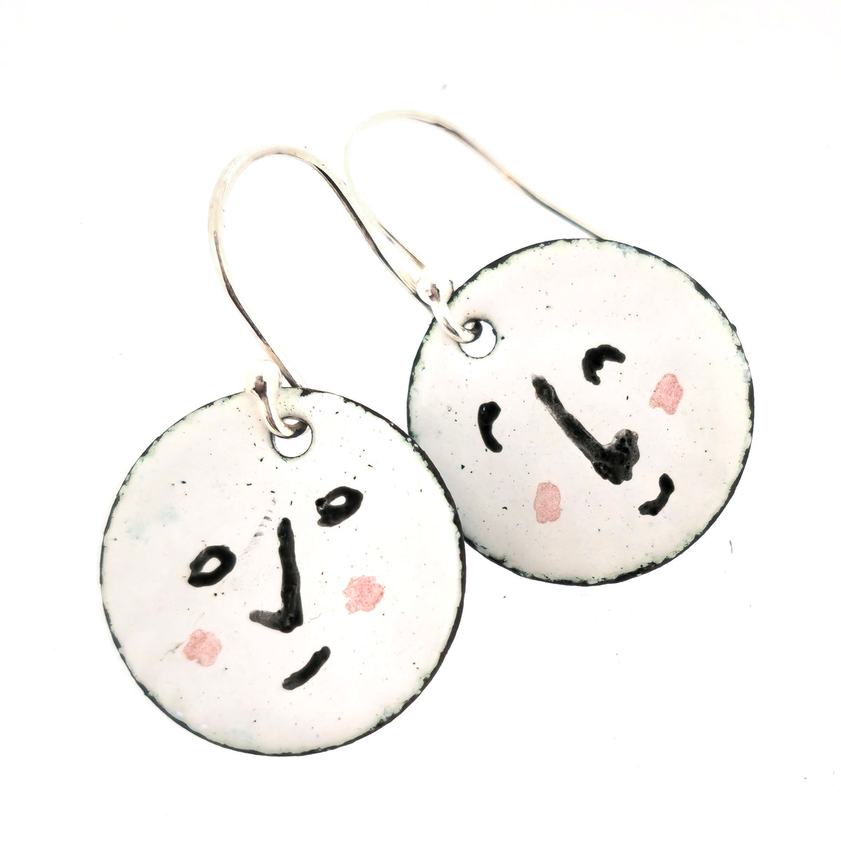 A pair of handmade enamel round drop earrings with a white background and different faces on each earrings in black and pink. On sterling silver ear hooks. Shown on a white background. Mijoux jewellery.