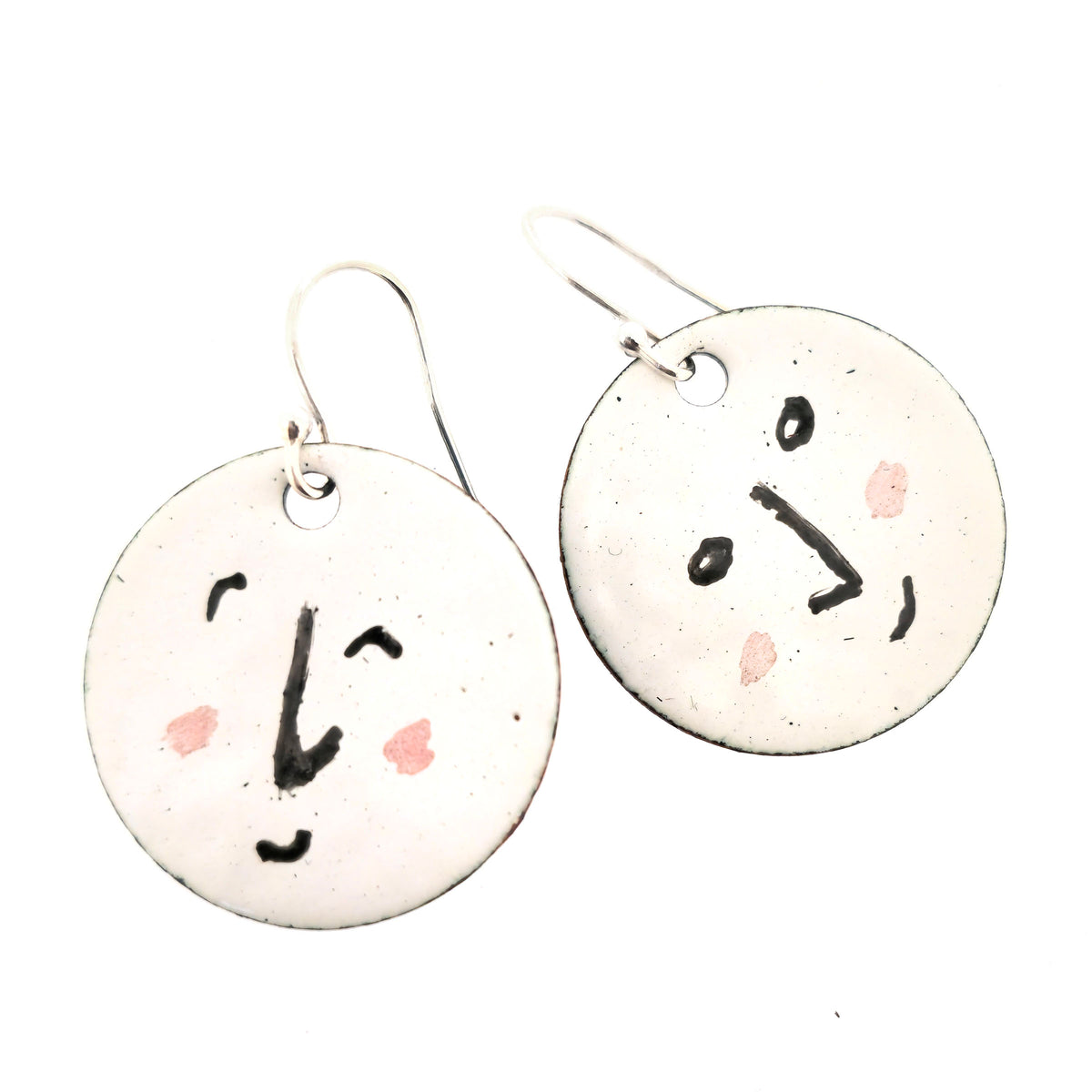 A pair of enamel round drop earrings with a white background and different faces on each earrings in black and pink. On sterling silver ear hooks. Shown on a white background. Mijoux jewellery.