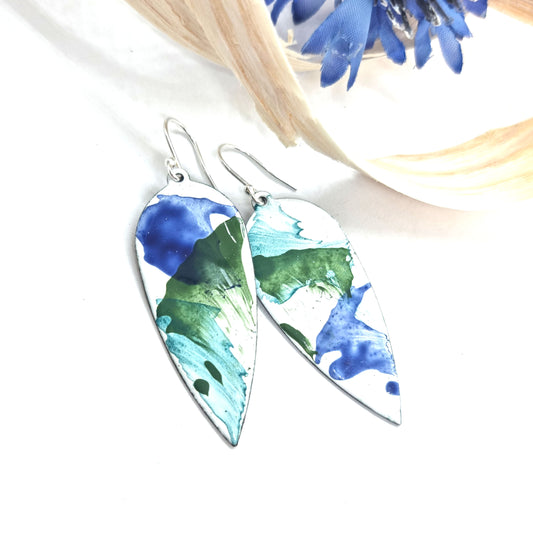 Large teardrop-shaped enamel drop earrings with splashes of dark blue and green on a white background - with flowers and wood shavings